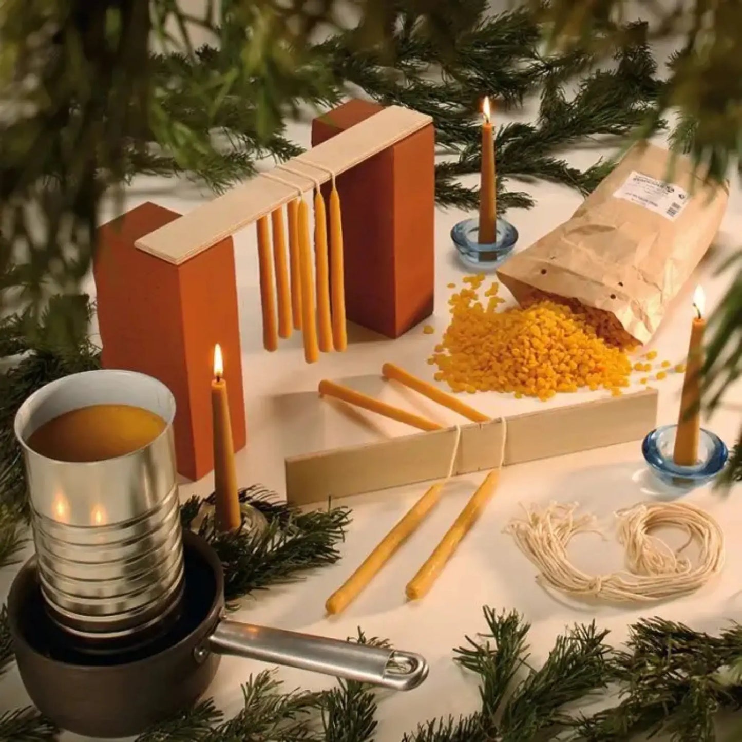 Candle-making kit with wicks, wax, and tools on a table with greenery.