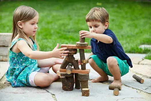 Two preschoolers playing with natural tree blocks outside