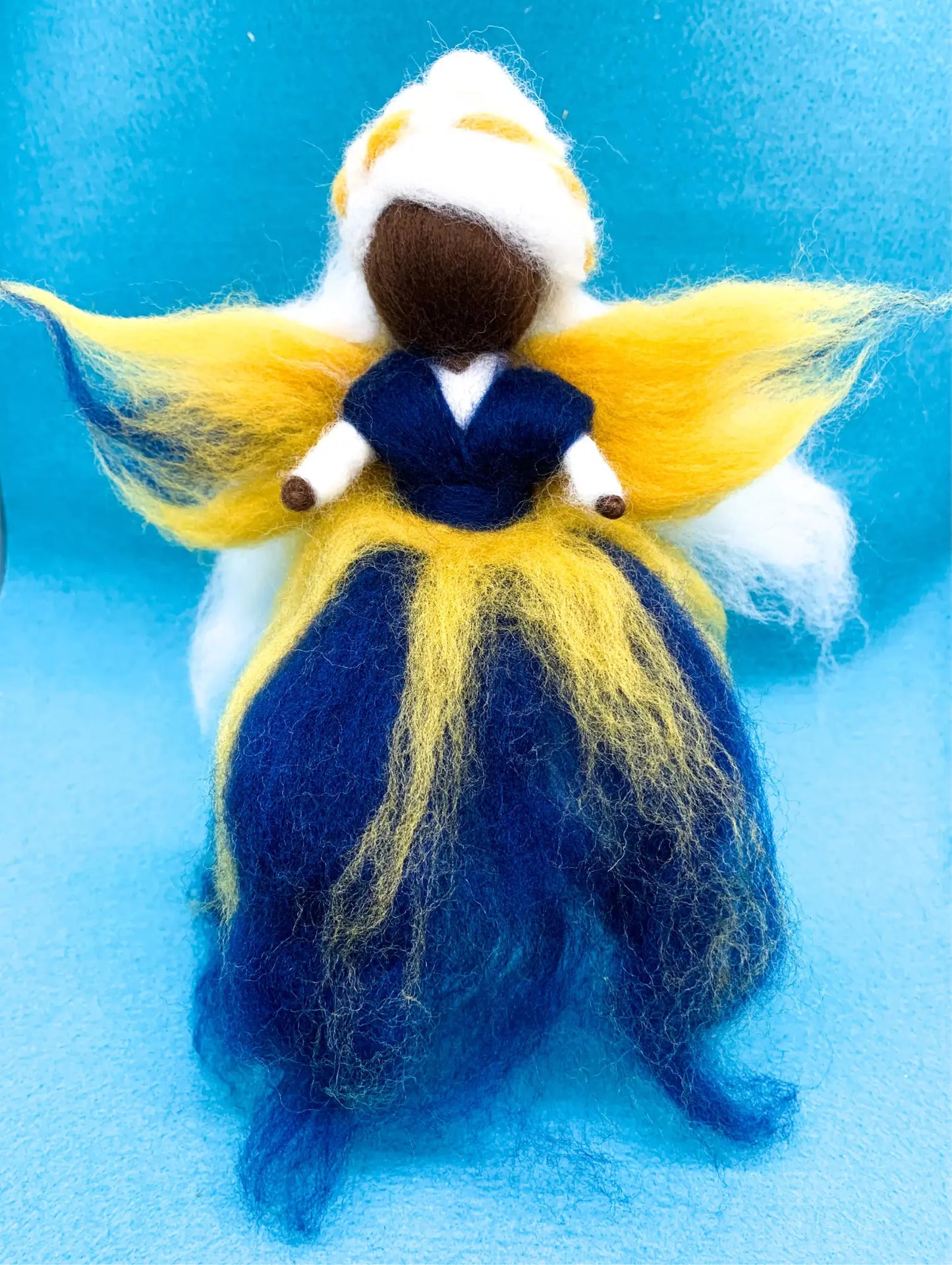 Felted fairy figurine with yellow hair and blue dress on a blue background