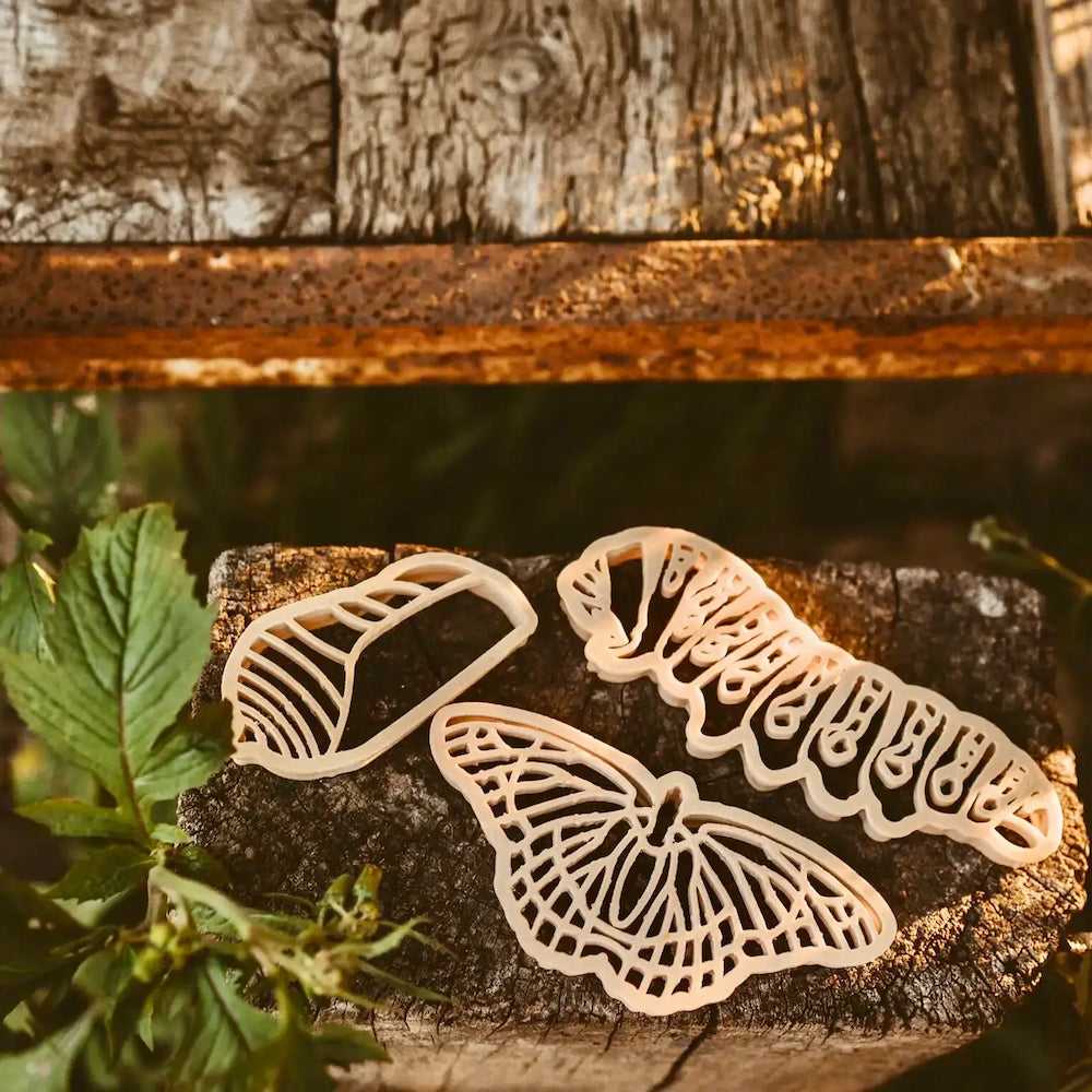 Three butterfly-shaped playdough cutters on a wooden surface with leaves in the background