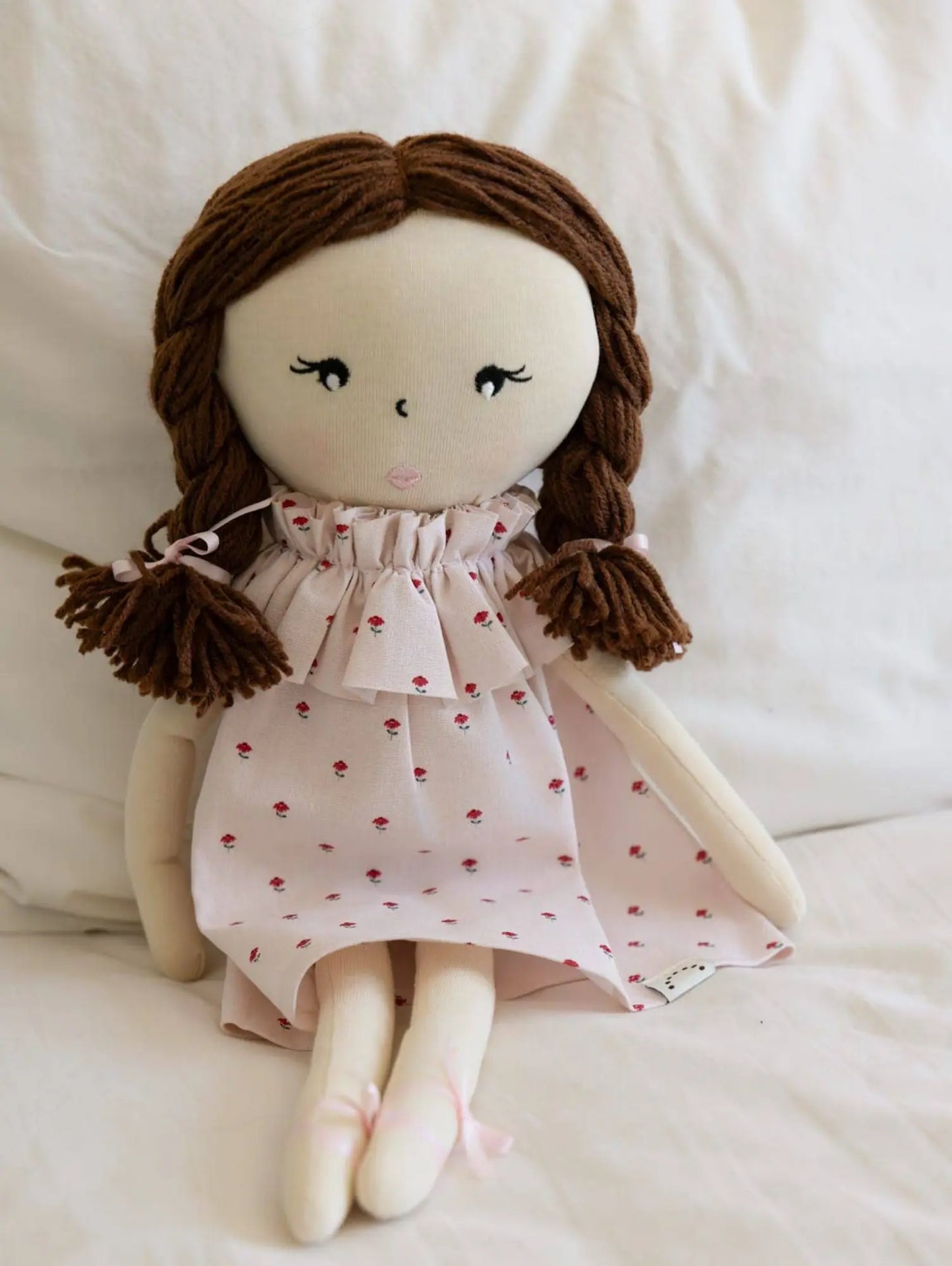 Handmade doll with brown hair and a pink dress with red patterns on a white background