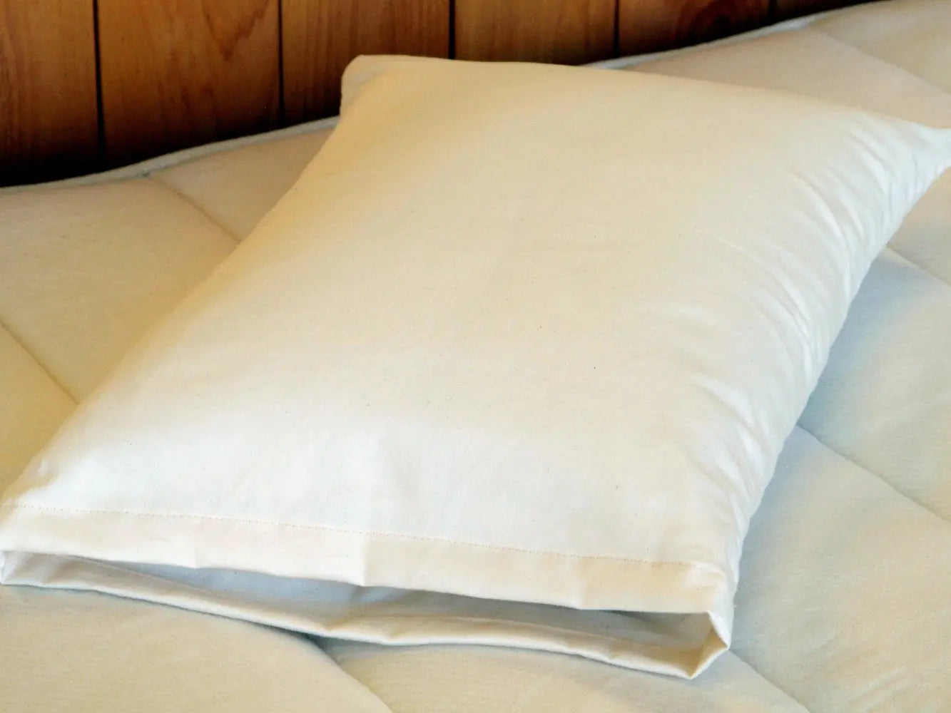 Close-up of a wool stuffed cotton covered pillow on a bed with a wooden headboard.