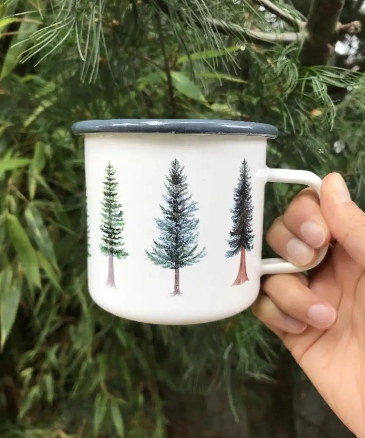 White mug with tree design held in front of green foliage