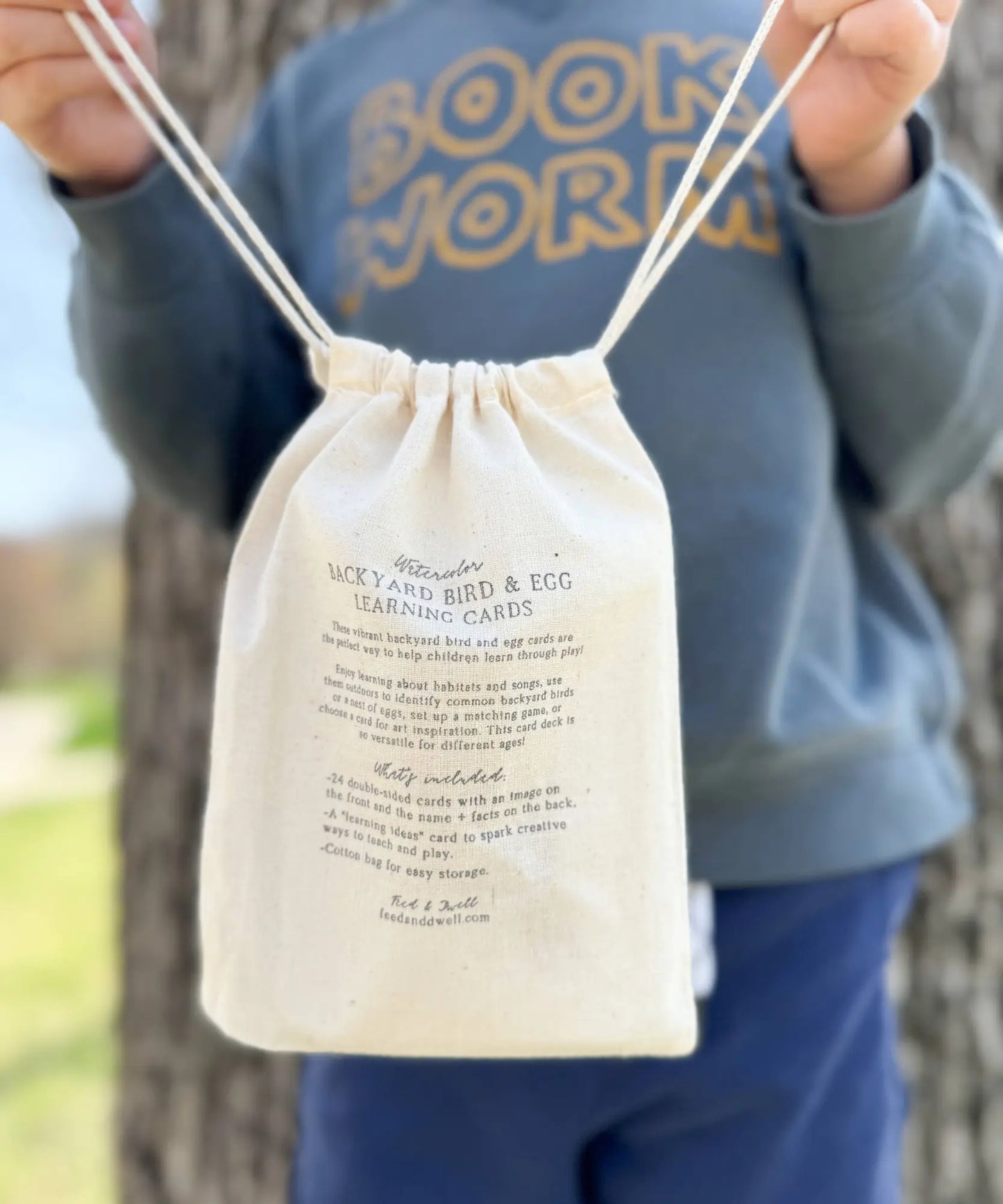 Child holding a Feed & Dwell Backyard bird and egg learning card drawstring bag