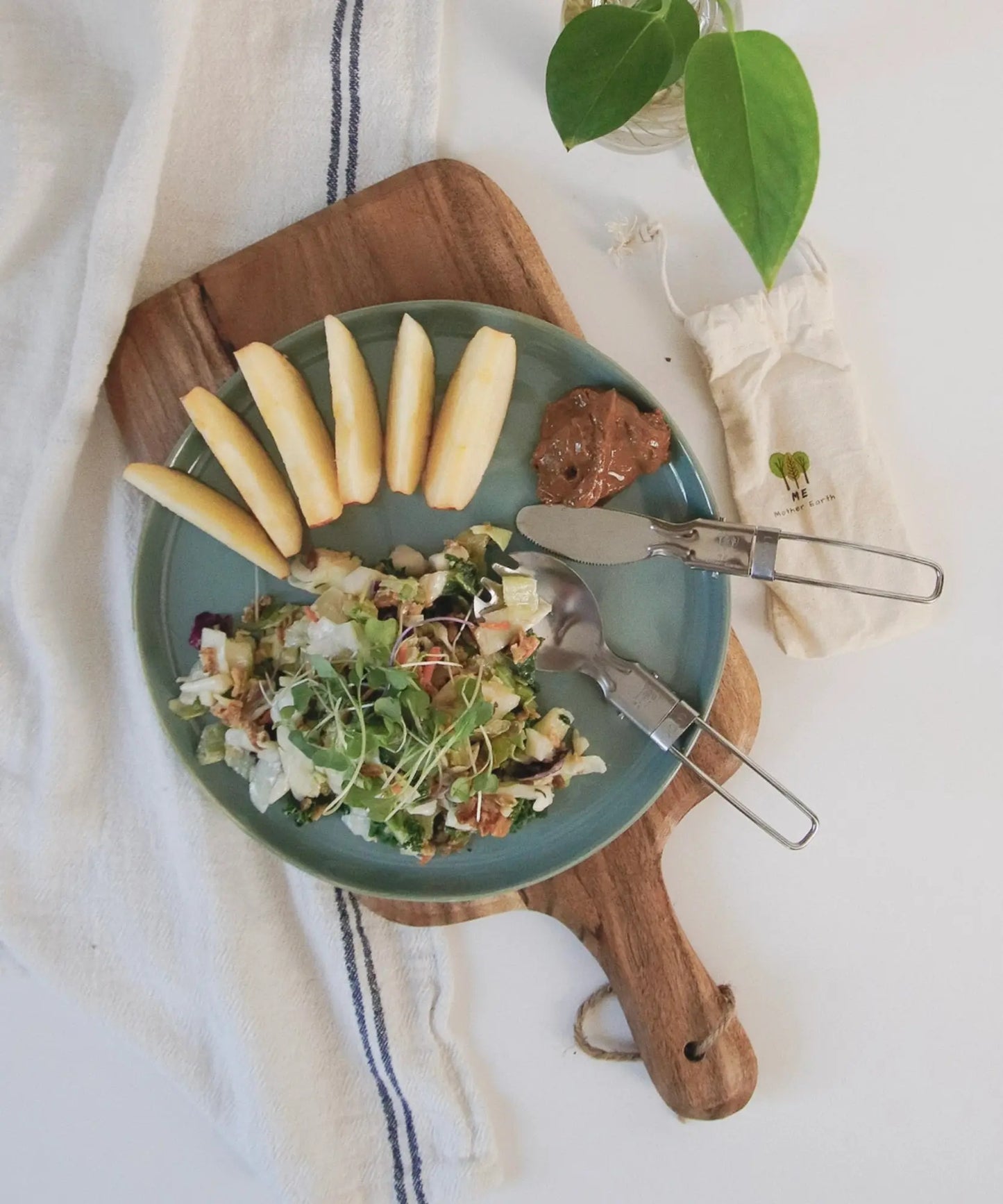 Green plate with salad, apples, and a spread on a wooden board.