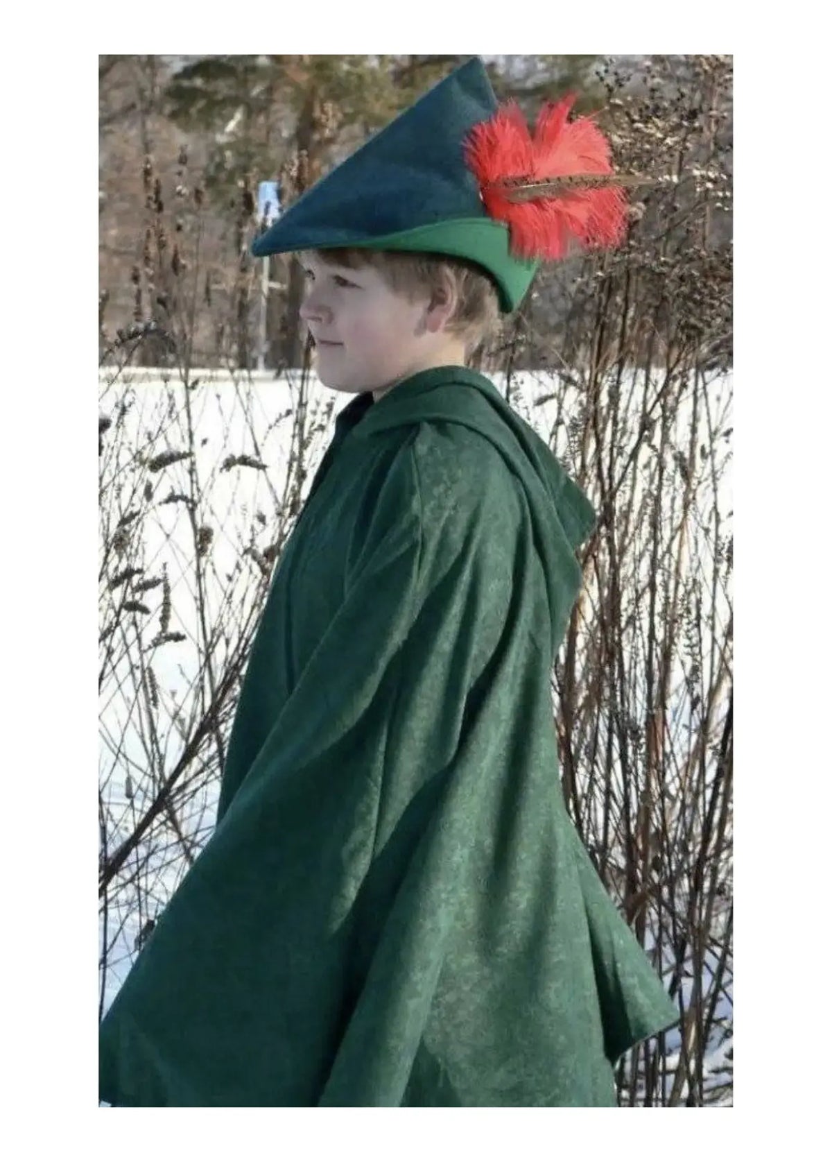 Child wearing a green woodsman cape costume with a red feather green hat in a snowy landscape