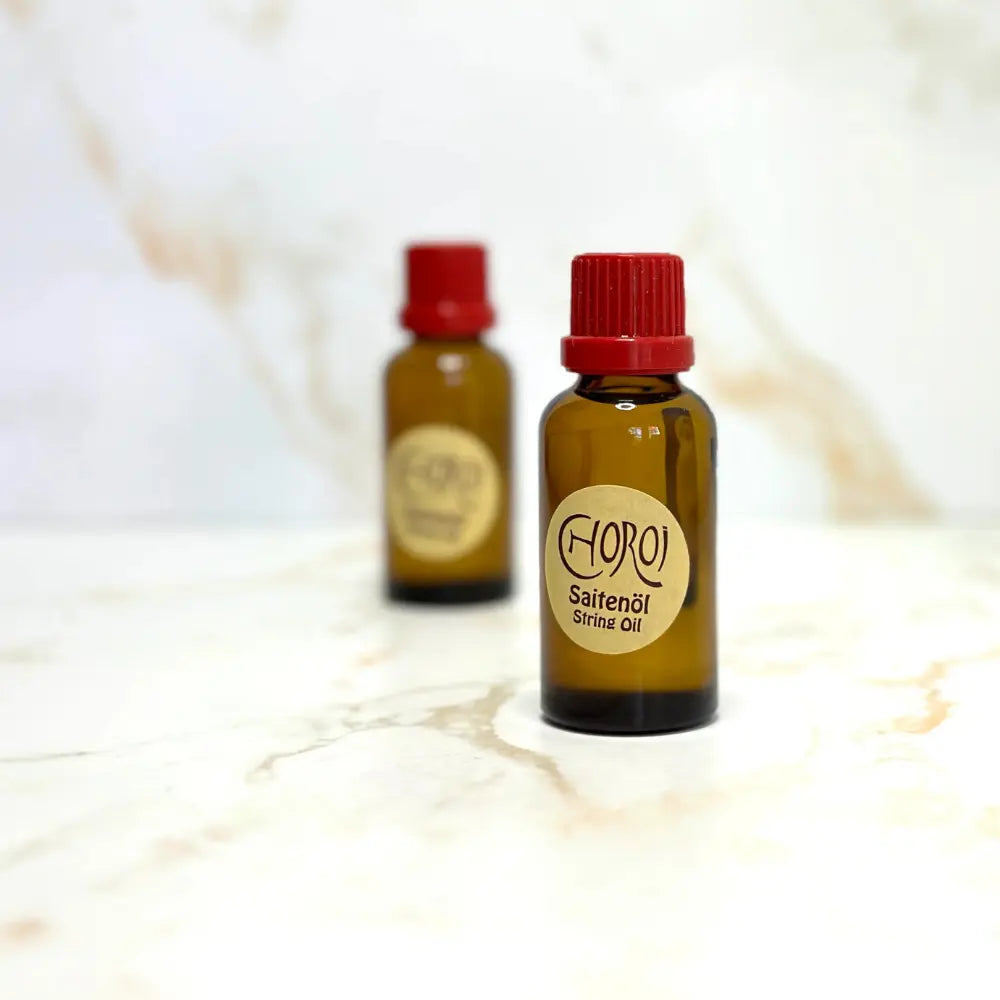 Two bottles of Choroi string oil with red caps on a marble surface.
