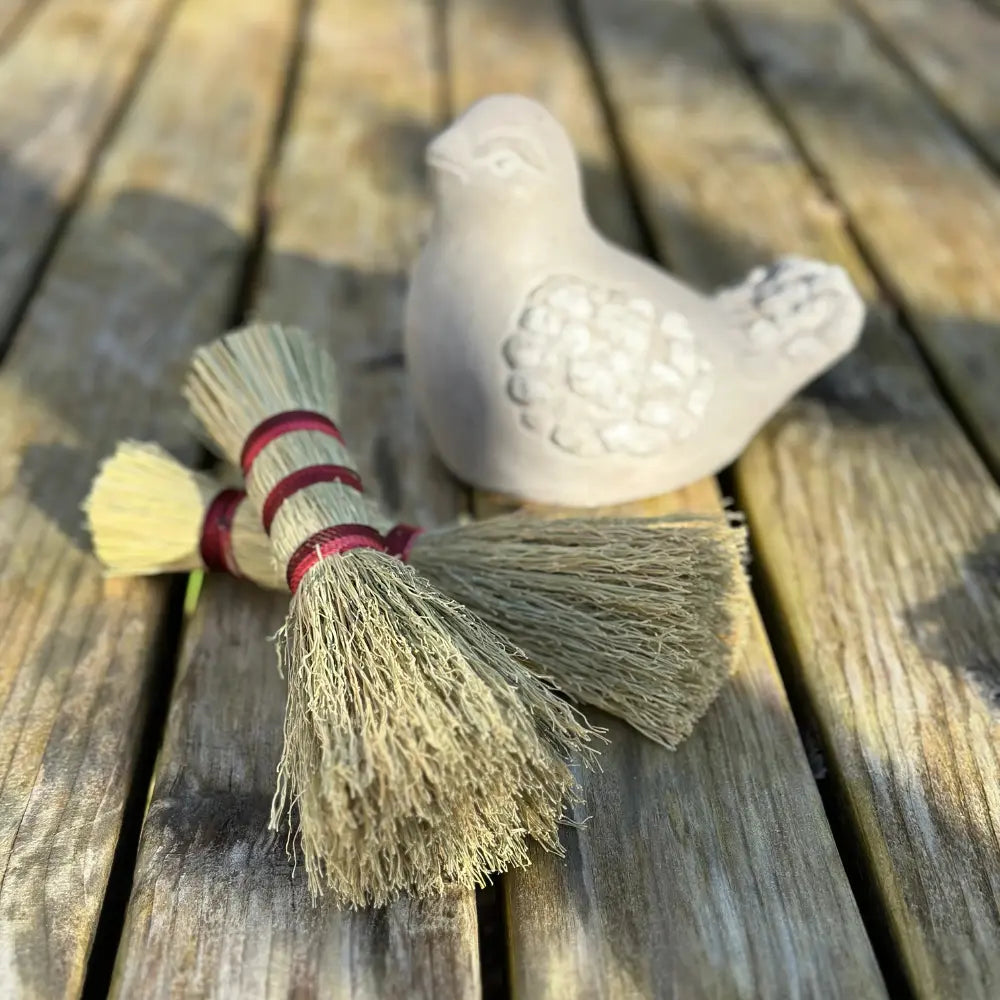 Small broom with a stone bird on a wooden surface