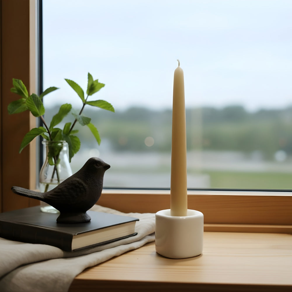 Candle in a white holder on a windowsill with a bird figurine and book nearby.