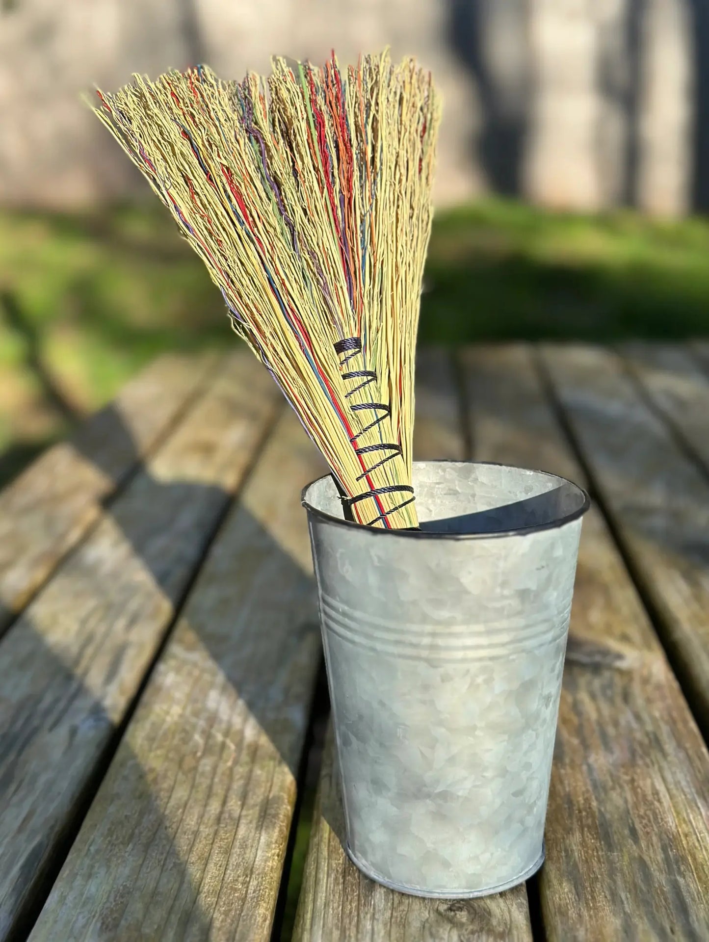 Bunch of dried plants in a metal cup on a wooden surface with a blurred natural background