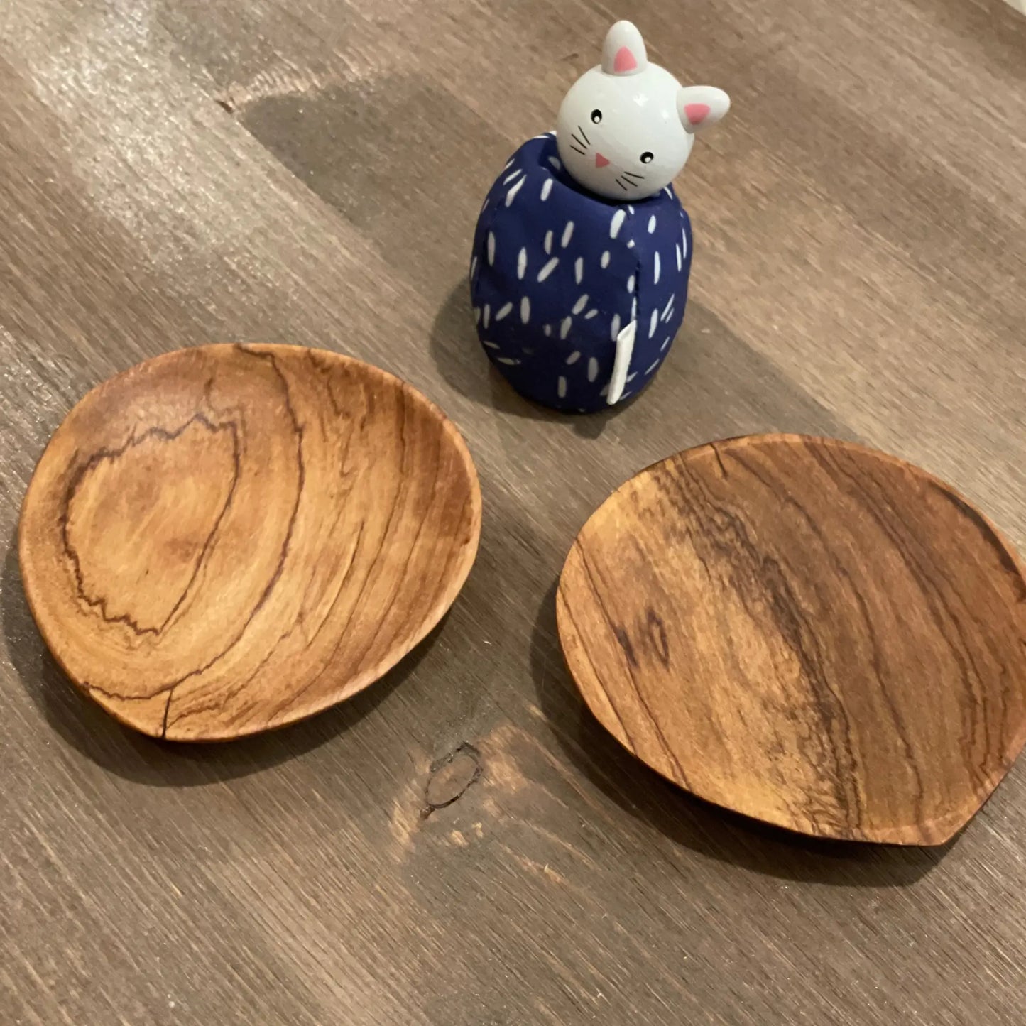 Two wooden coasters on a wooden surface with a small ceramic cat figurine.