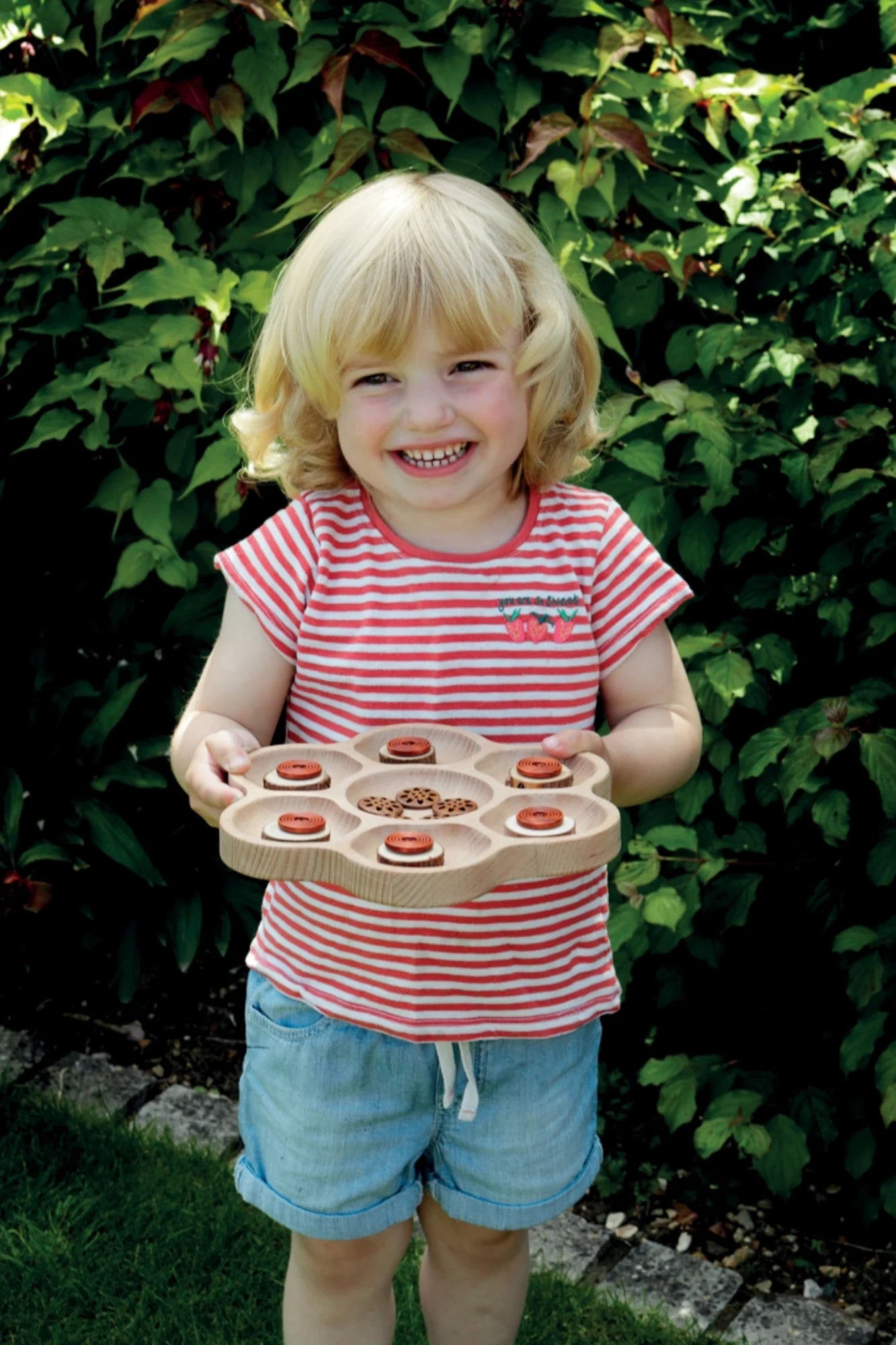 A young child smiling holding a nature sorting tray with outside background
