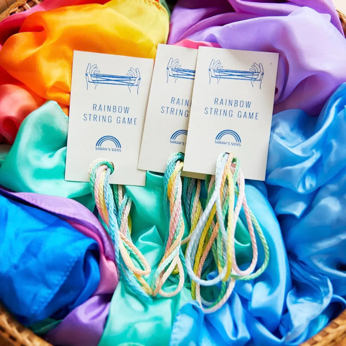 Three Sarah’s Silks rainbow string games displayed on colorful Playsilks