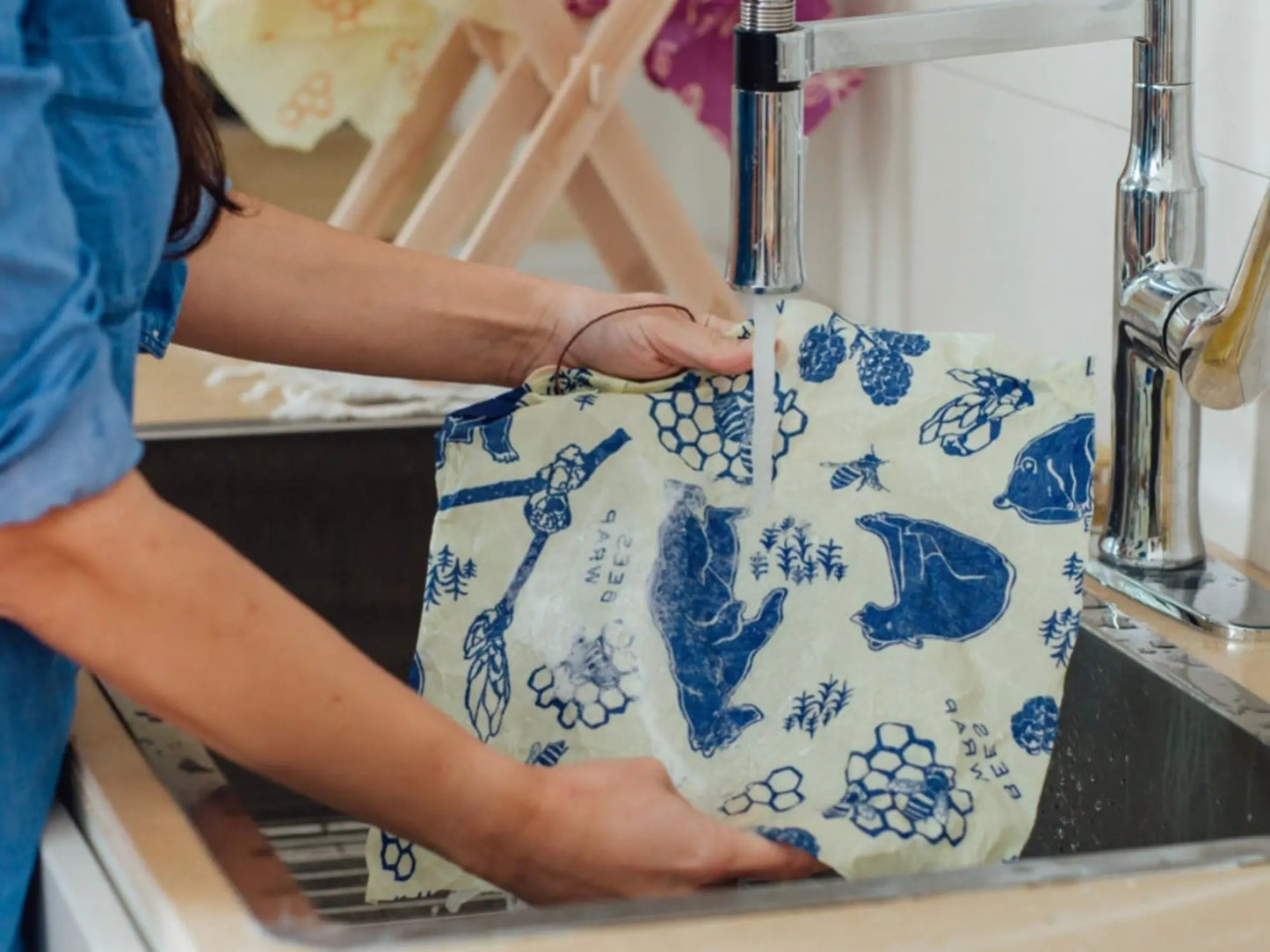 Person washing a blue and white patterned beeswax wrap in a sink with running water.