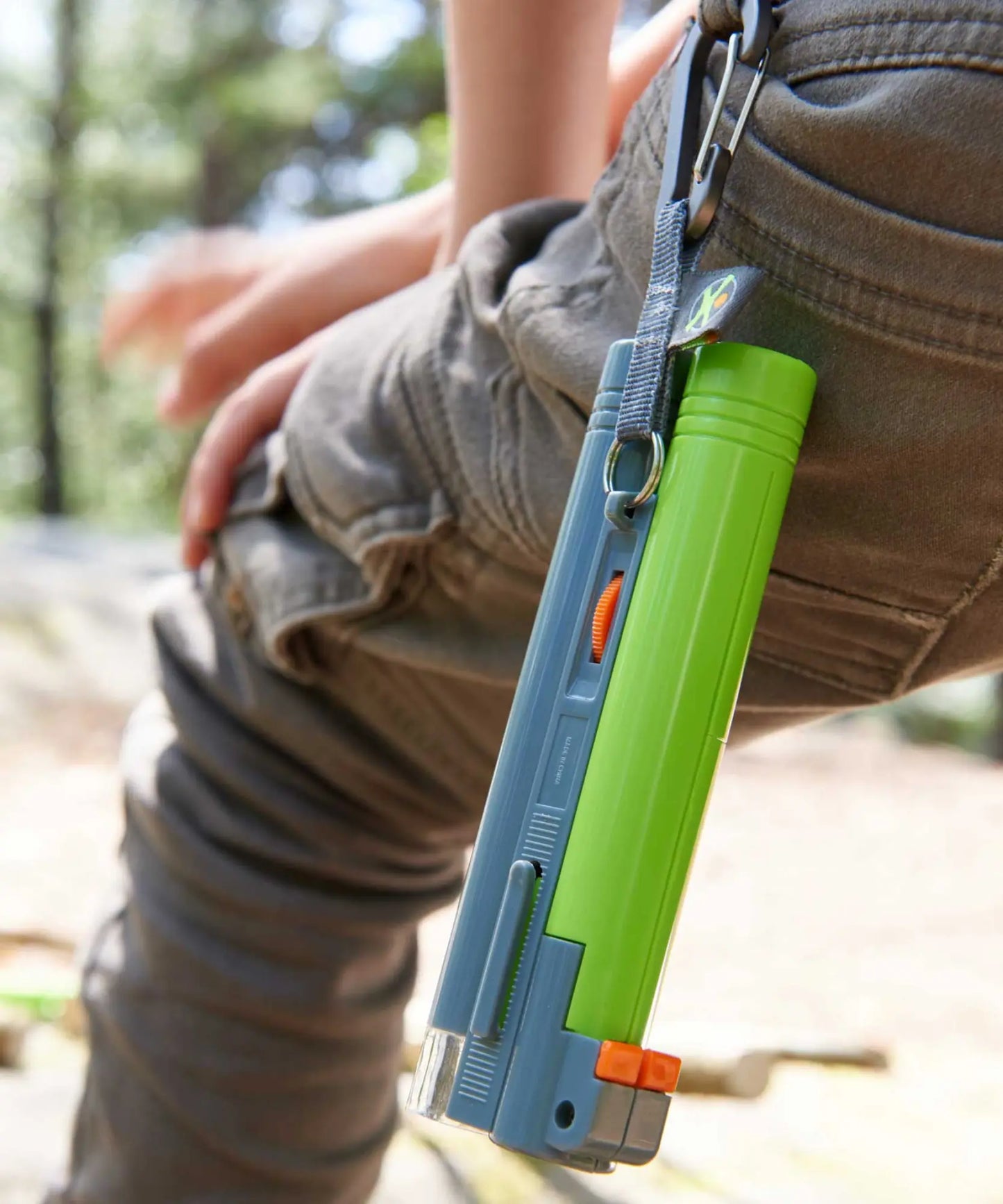 Green and blue tool attached to a person's pants with a blurred natural background