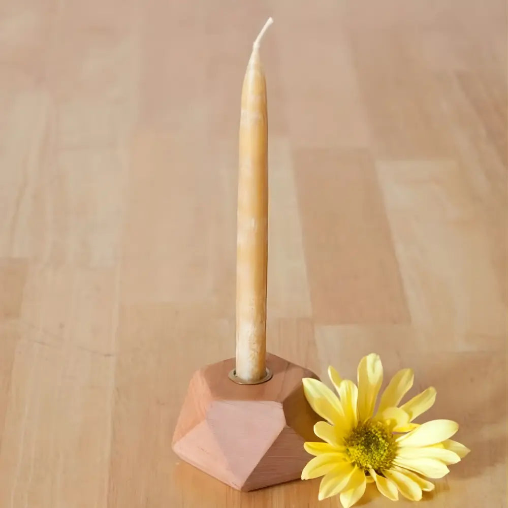 Candle in a geometric holder with a yellow flower on a wooden surface