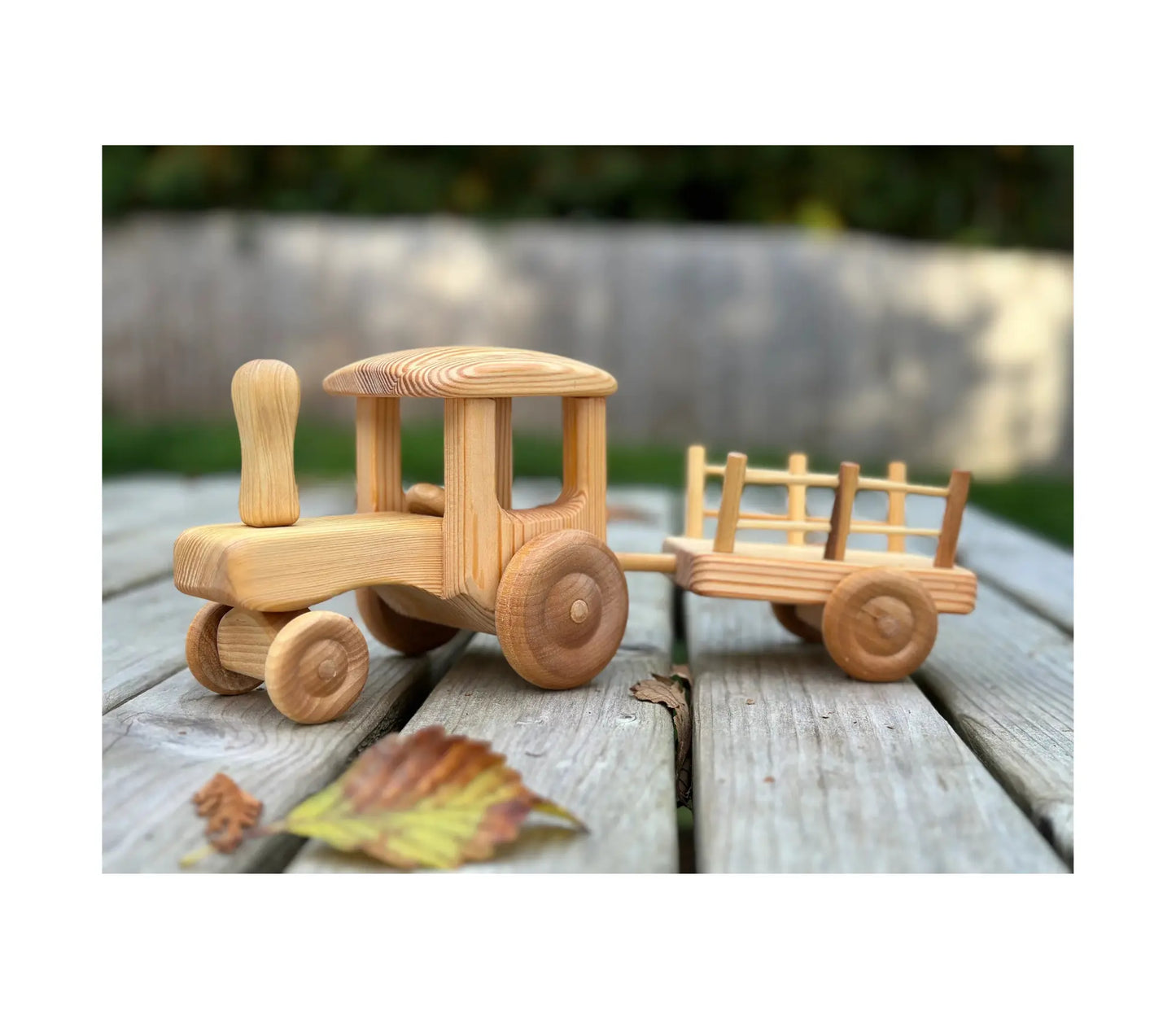 Wooden tractor with trailer by Telleby outdoors on wooden surface with autumn leaves showing natural play setting