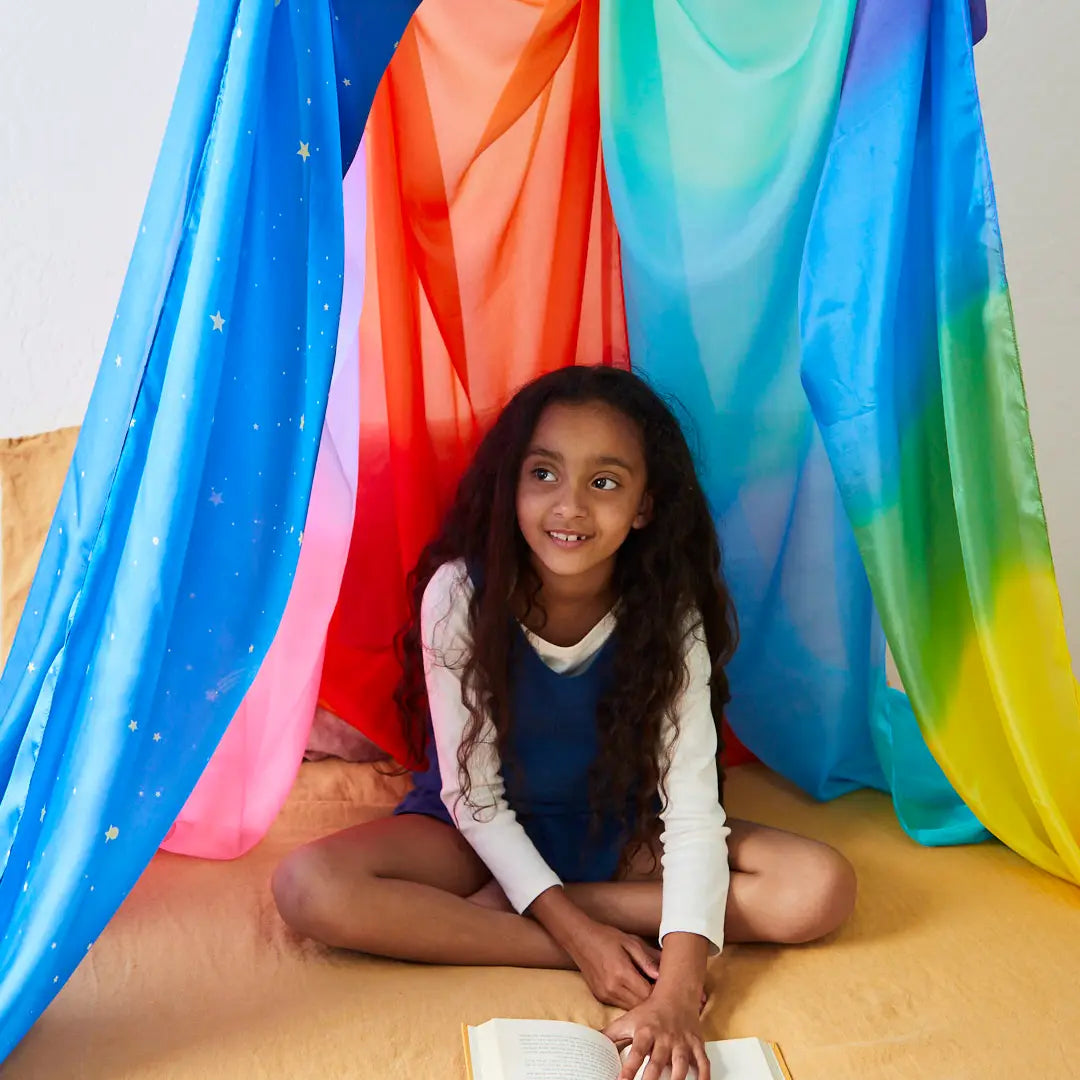 Girl sitting on floor surrounded by multiple colorful giant playsilks tied to ring hanging from ceiling