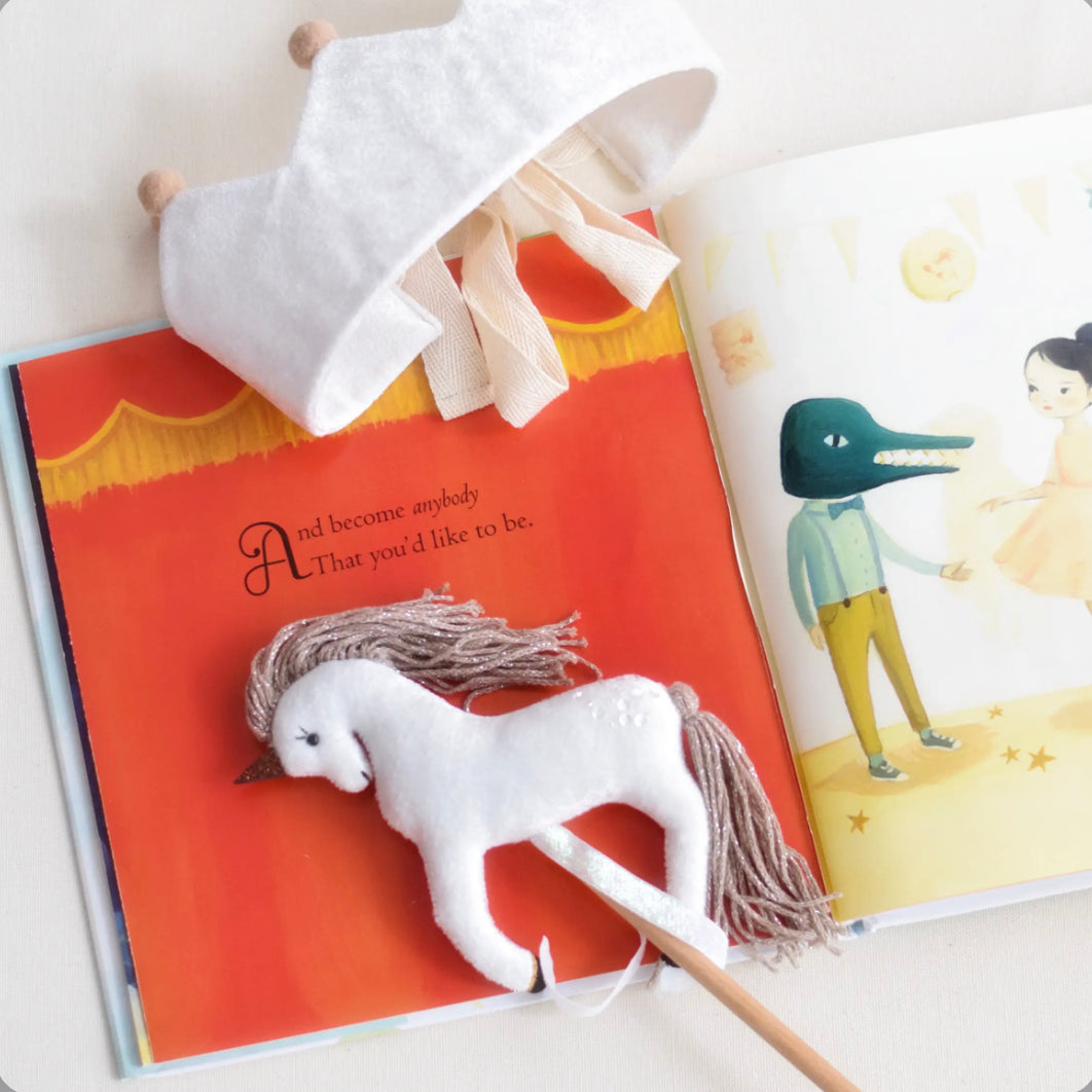 A Velvet Unicorn Wand with ribbons and matching crown laying on top of a picture book