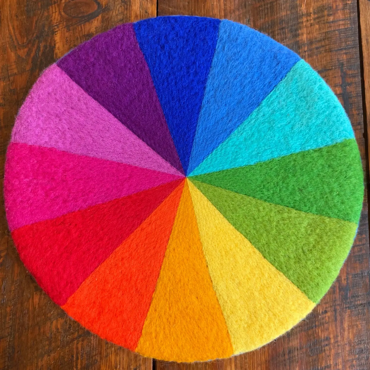 12-color rainbow felt play mat photographed on a wooden table