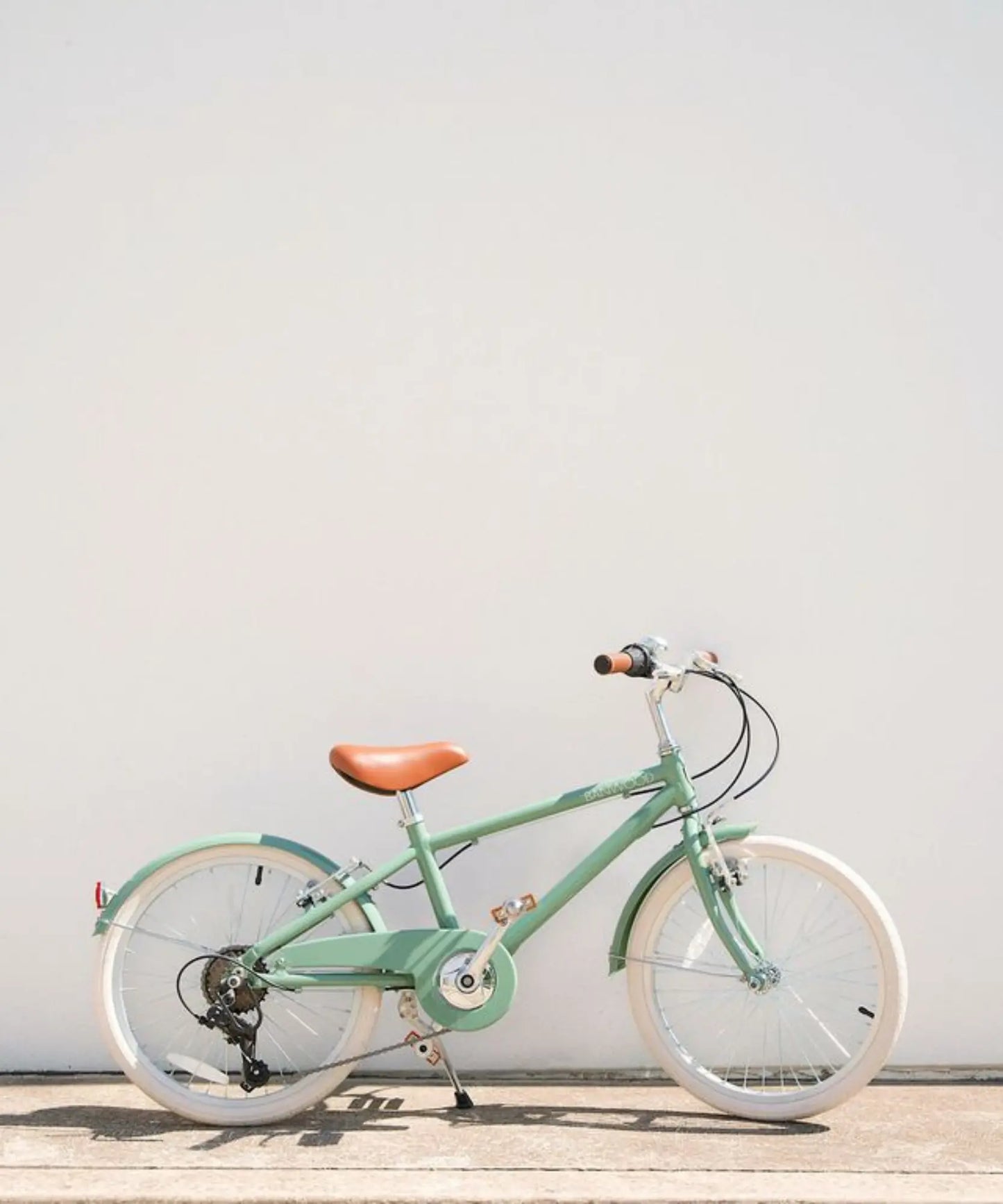 Green 20 inch bicycle with a brown seat on a light wooden floor against a white wall