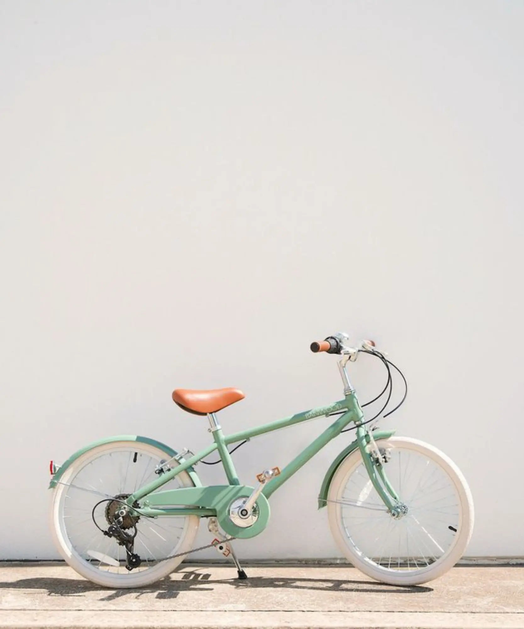 Green 20 inch bicycle with a brown seat on a light wooden floor against a white wall