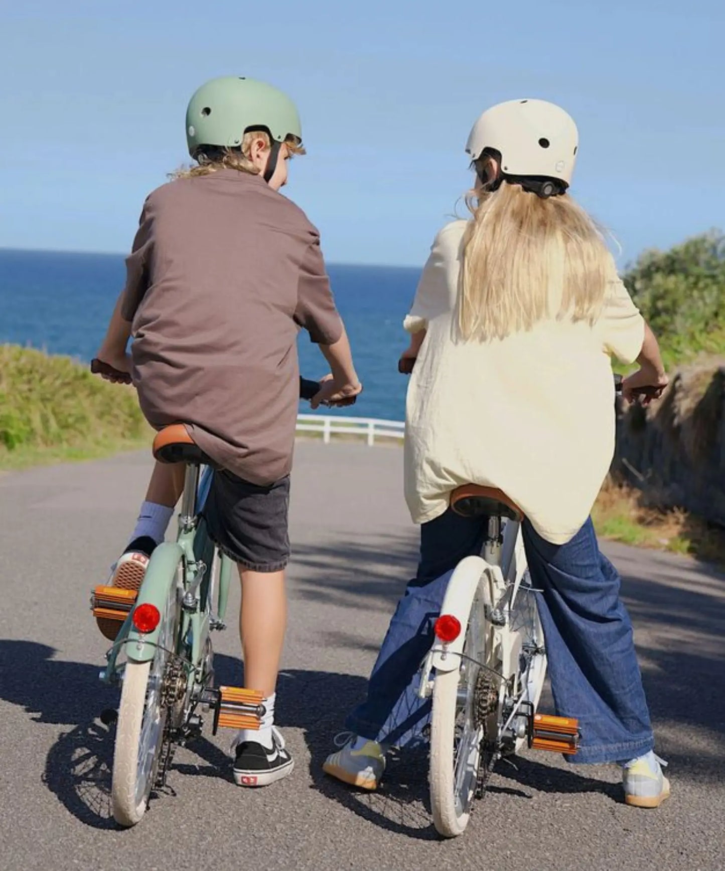 Two children riding bicycles on a road with an ocean view