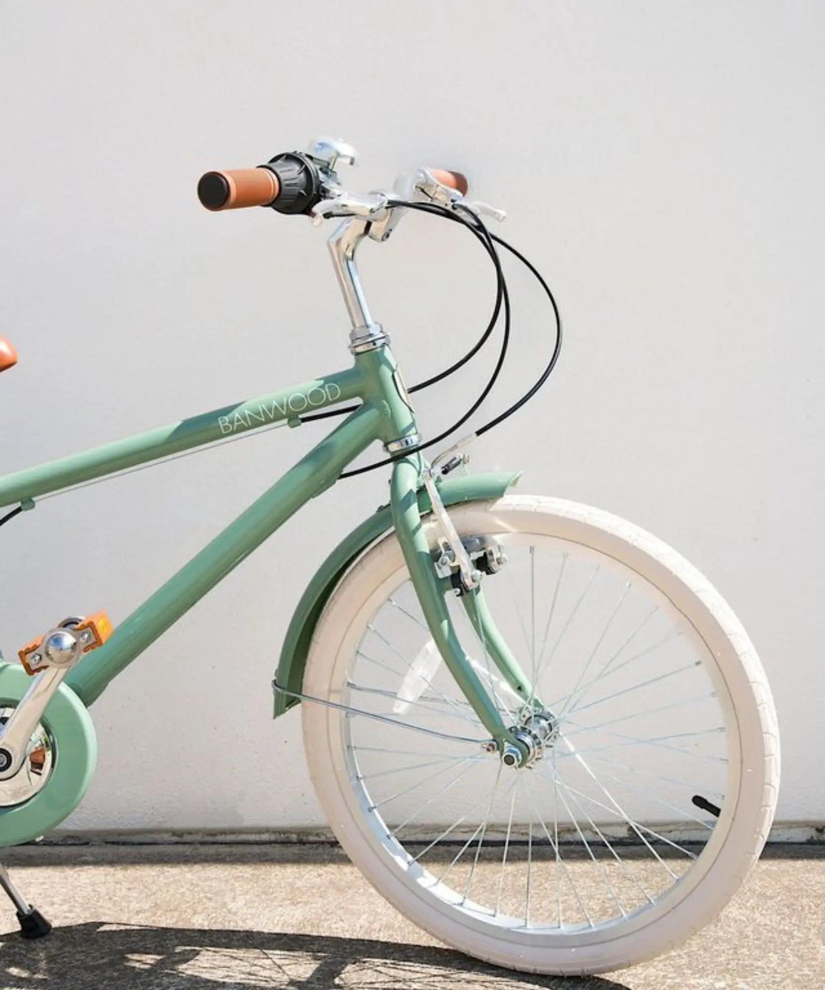 Green kids bicycle with brakes with white wheels against a light gray background