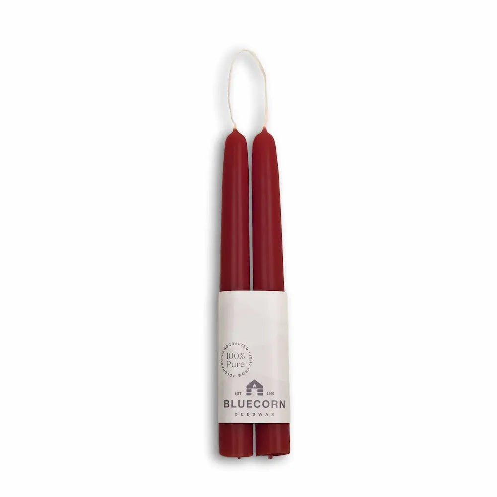 Two burgundy candles in a white cylindrical holder with 'Bluecorn' branding on a white background