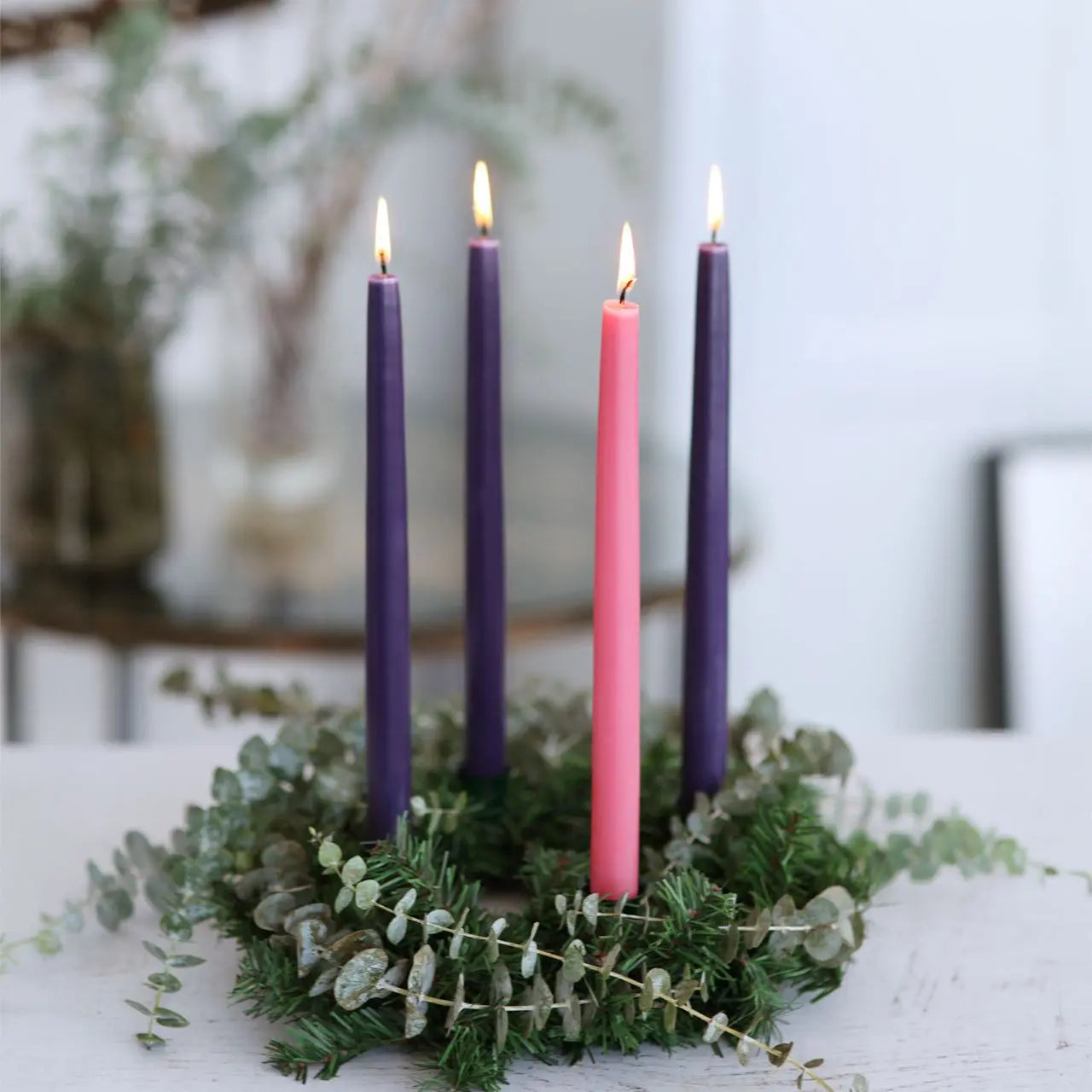 Advent wreath with four candles, three purple and one pink, on a white surface.