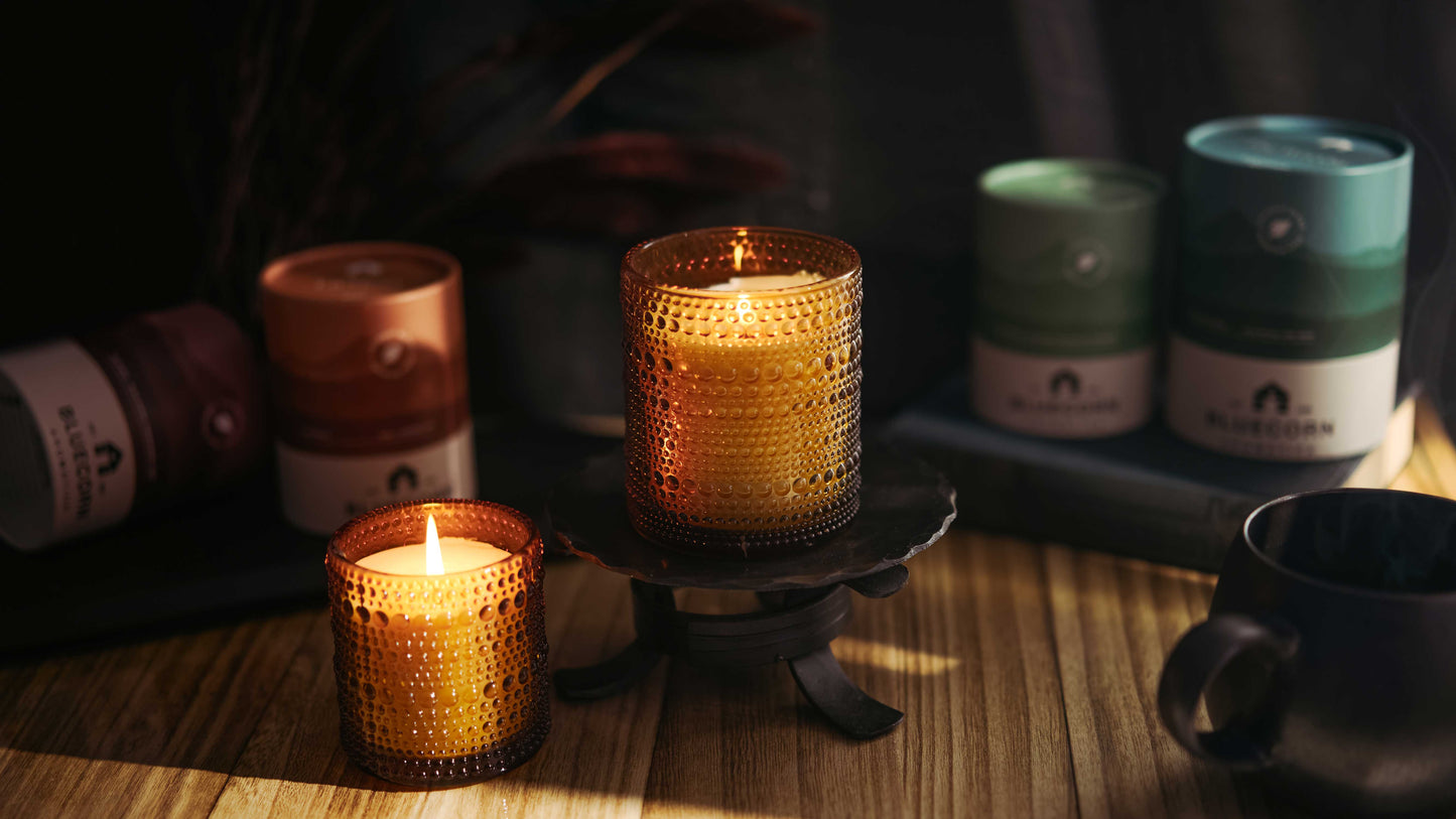 Candlelit scene with textured candles on a wooden surface, surrounded by bottles and a cup.