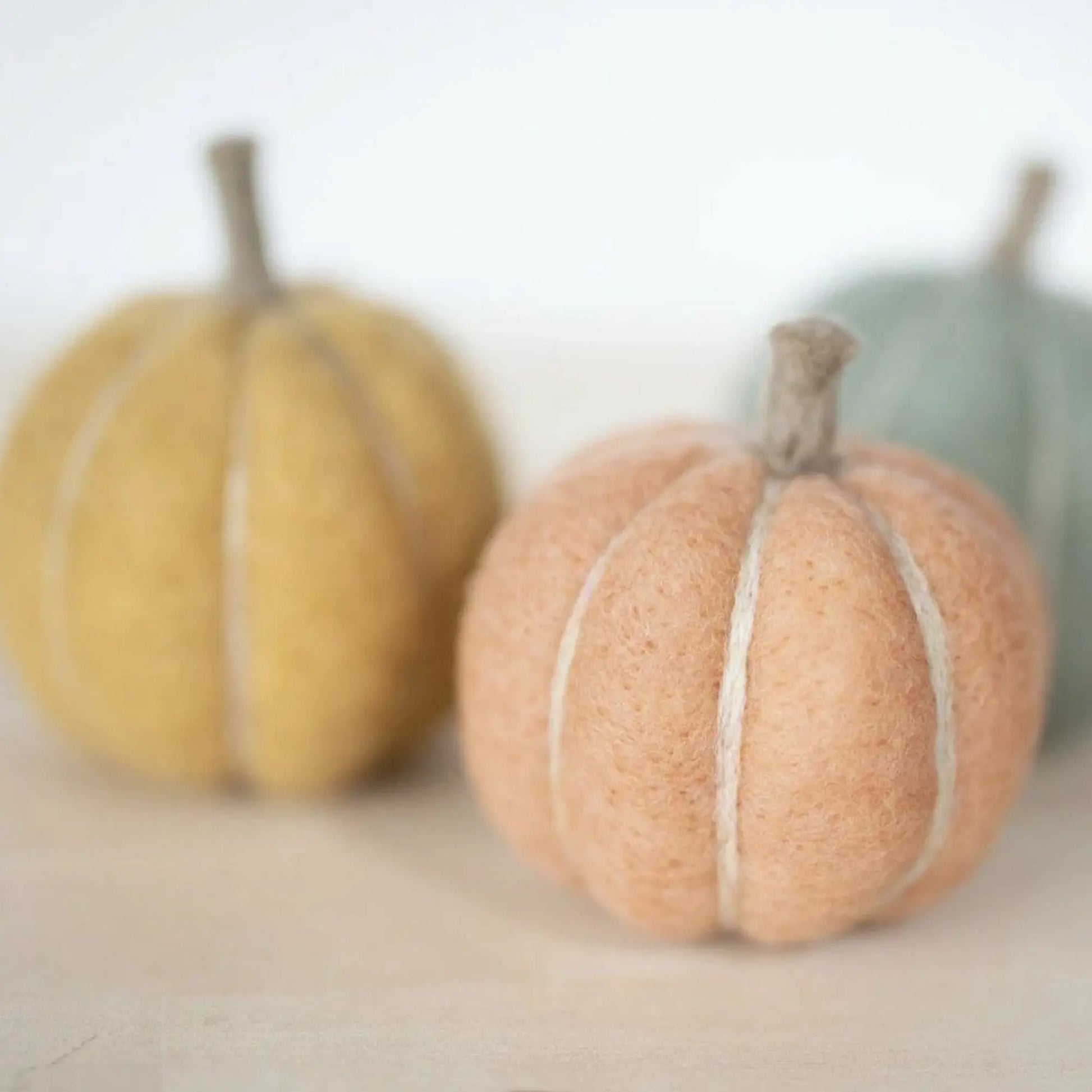 Three decorative pumpkins in yellow, orange, and green on a neutral background