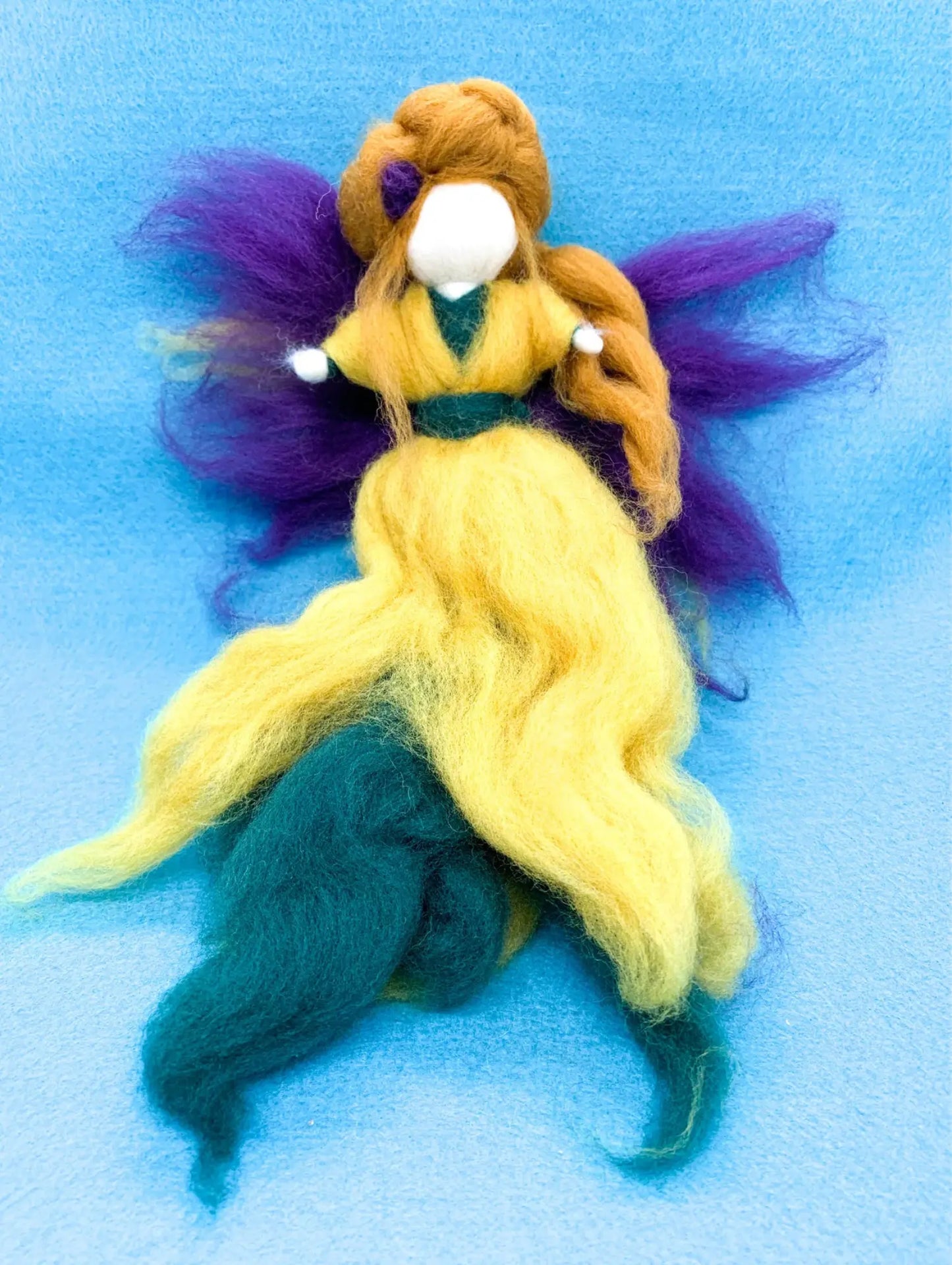 Wool Fairy doll with yellow over green dress, purple wings, and light brown hair with purple flower on blue background