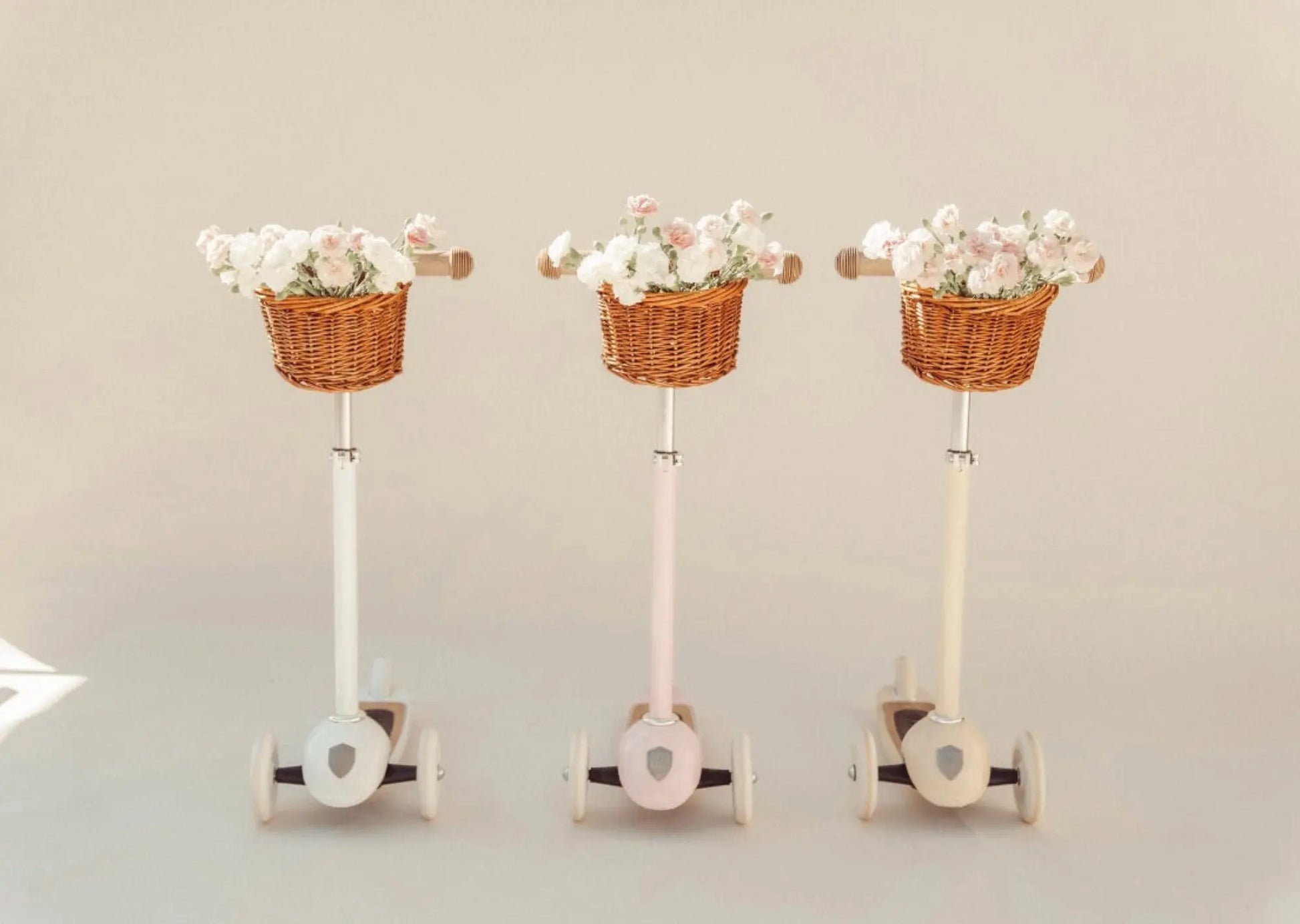 Banwood Three Wheel Scooters side by side in white, pink and cream with baskets filled with flowers