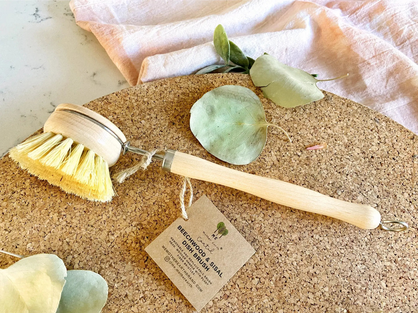 Two wooden scrub brushes on a cork board with eucalyptus leaves and a tag.