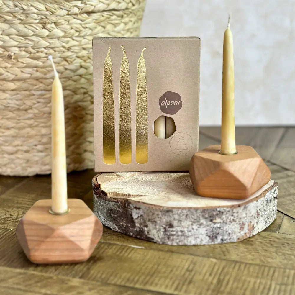 Two wooden candle holders with candles on a wooden surface, featuring a box of dipam candles in the background.