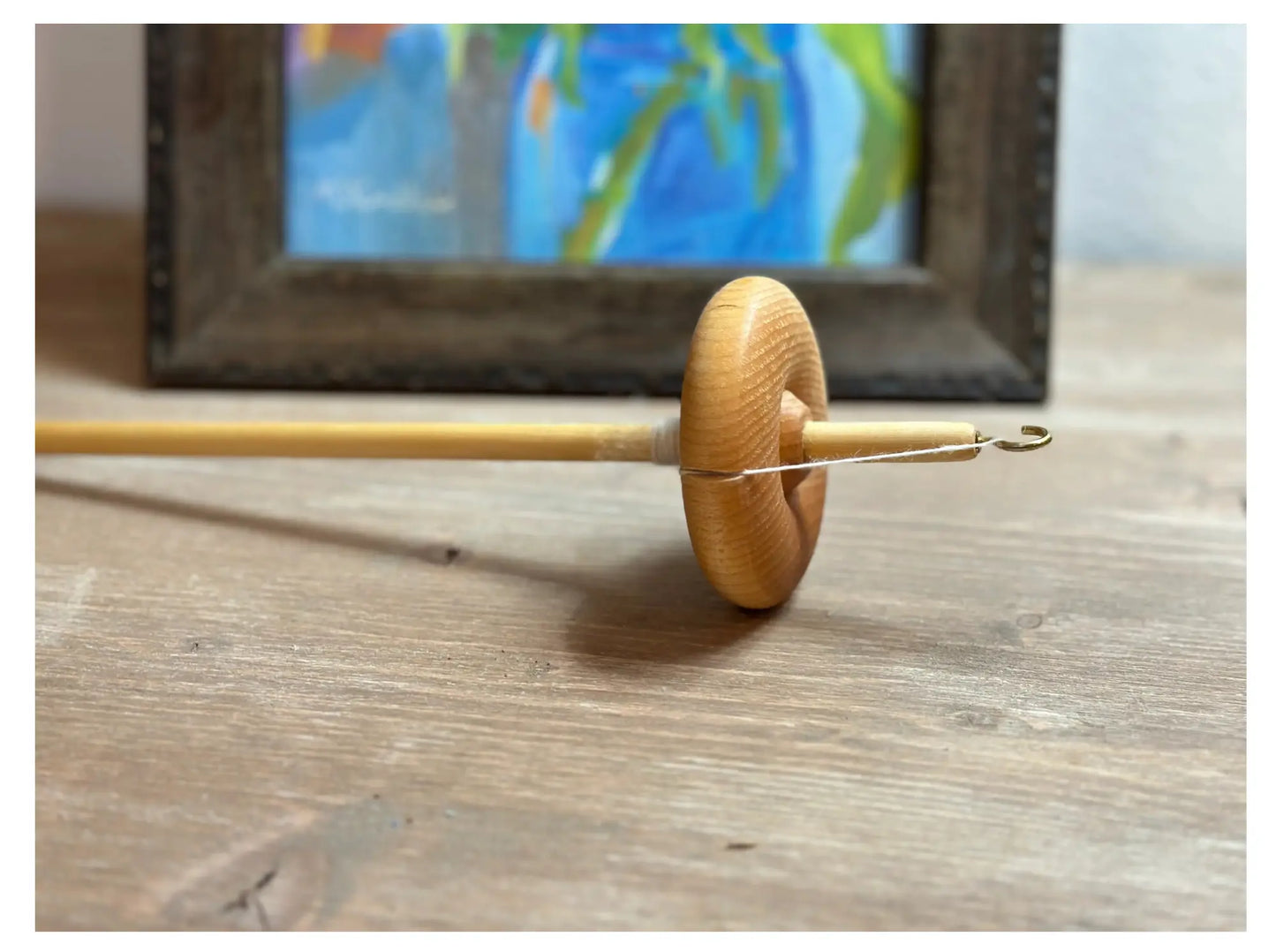 A Wooden Drop Spindle - Top Whorl; High Whorl Spindle - on a wooden surface