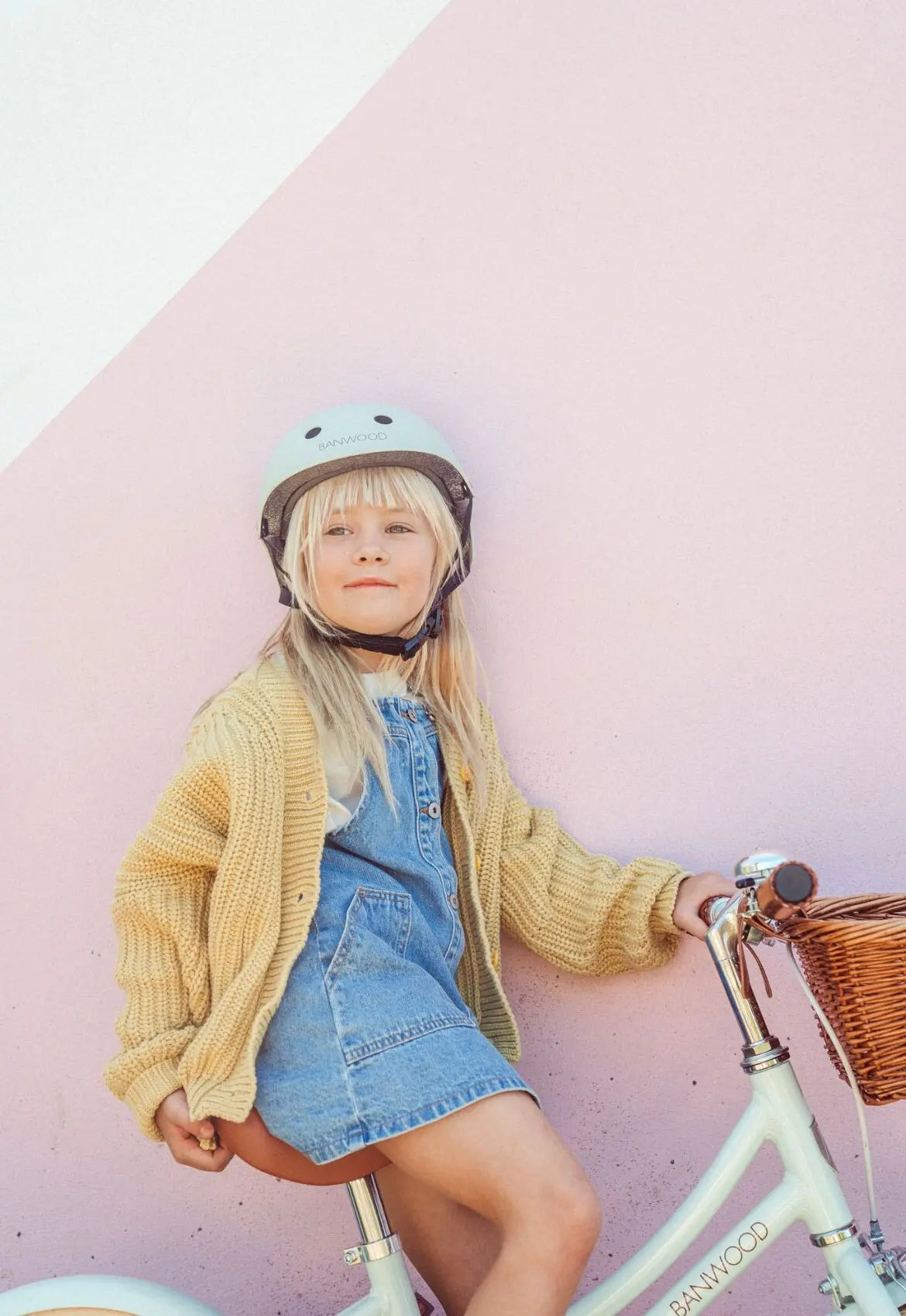 Child with a bicycle wearing a helmet against a pink background