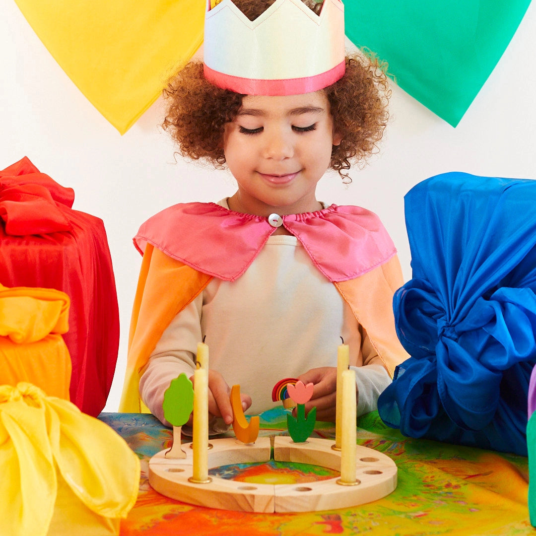 Child in colorful costume playing with wooden charms on her birthday ring, surrounded by colorful gifts