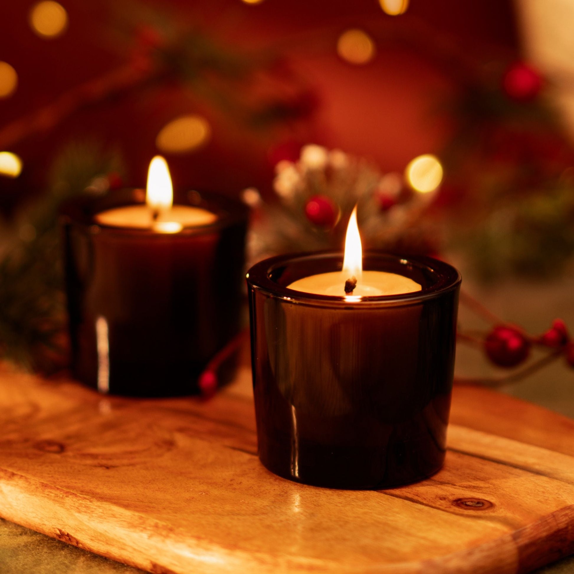 Two lit candles in dark holders on a wooden surface with a festive background.