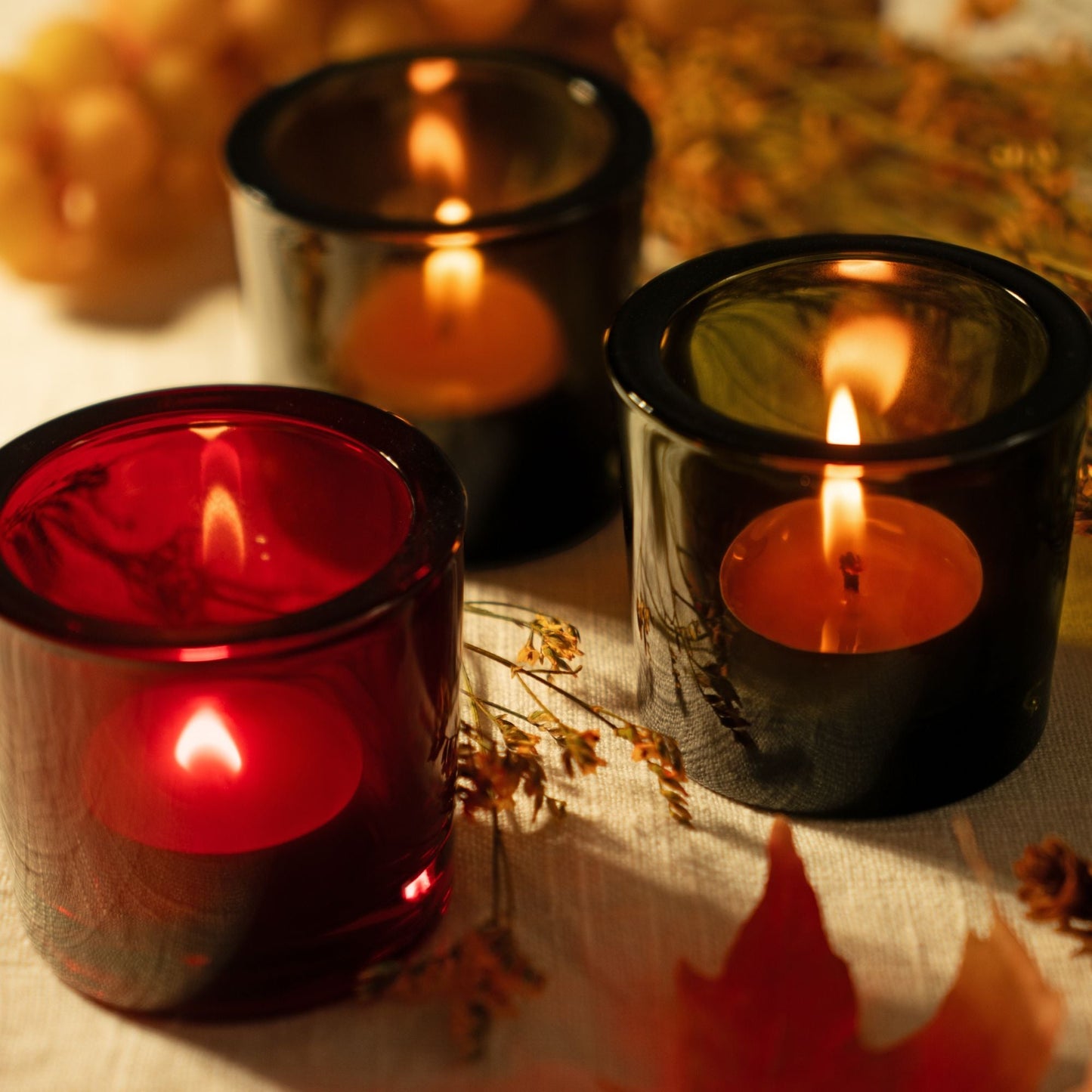 Three lit candles in black holders on a surface with autumn decorations.