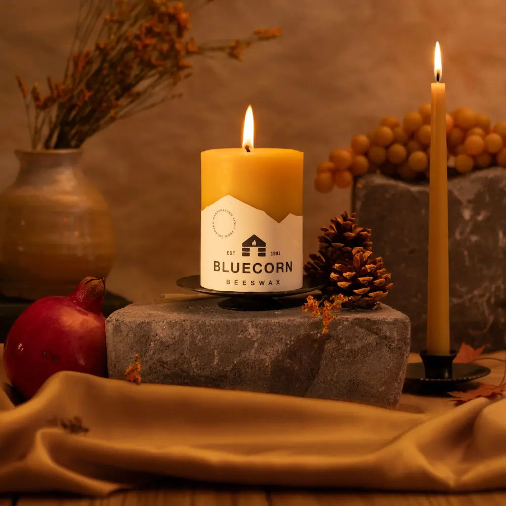 Candle with 'Bluecorn Beeswax' label on a stone block with decorative elements.