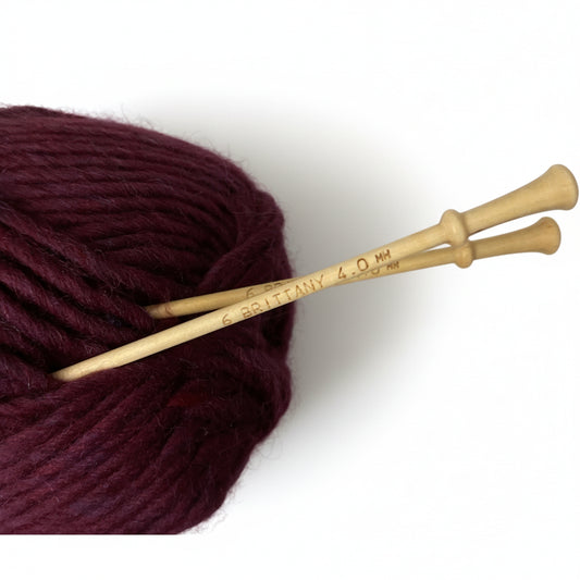 Brittany Single Point Wooden Knitting Needles in a skein of maroon yarn on white background
