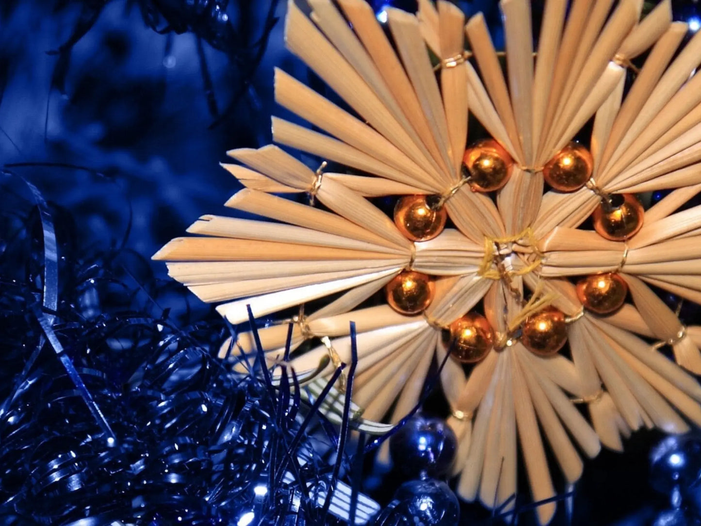 Woven ornament from straw with copper beads on a blue tinsel background