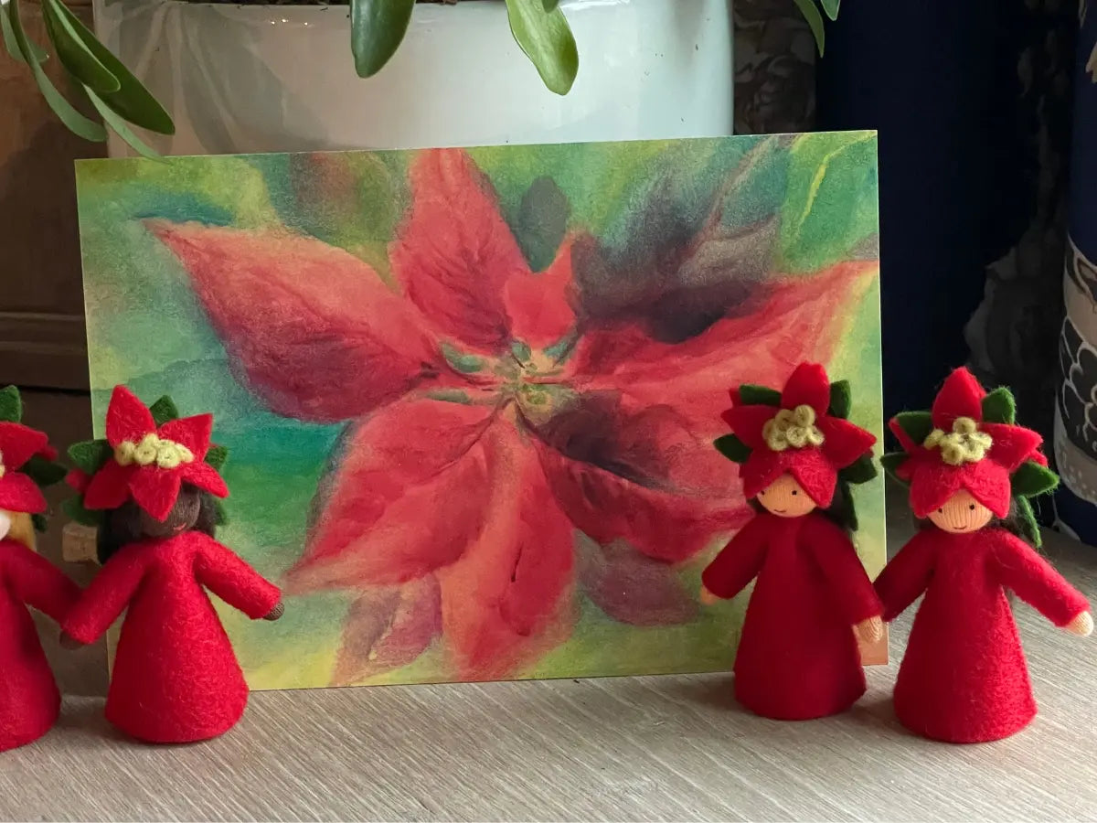 Red flower-shaped figures with green leaves in front of a painting of a red poinsettia flower.