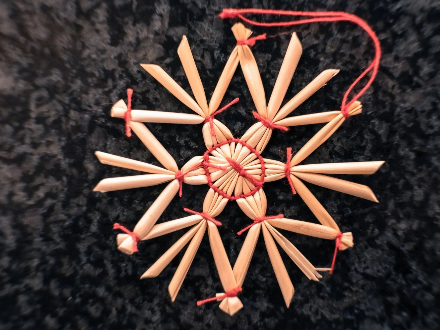 Decorative straw star ornament with red string on a dark background