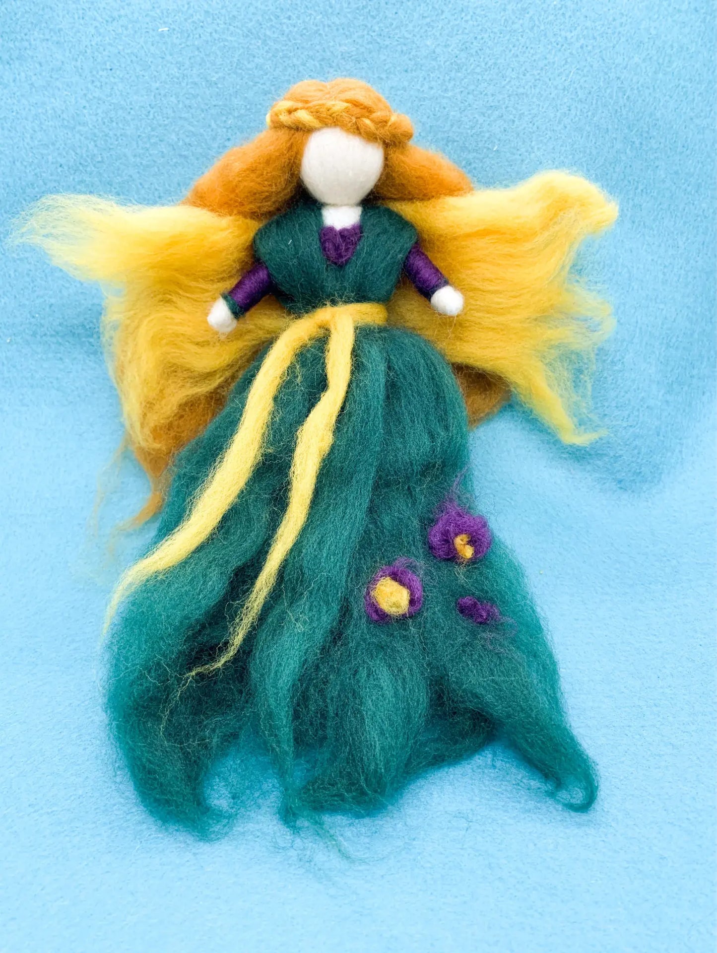 Wool Fairy doll with green dress, purple flowers, golden yellow wings, and light brown hair on a blue background