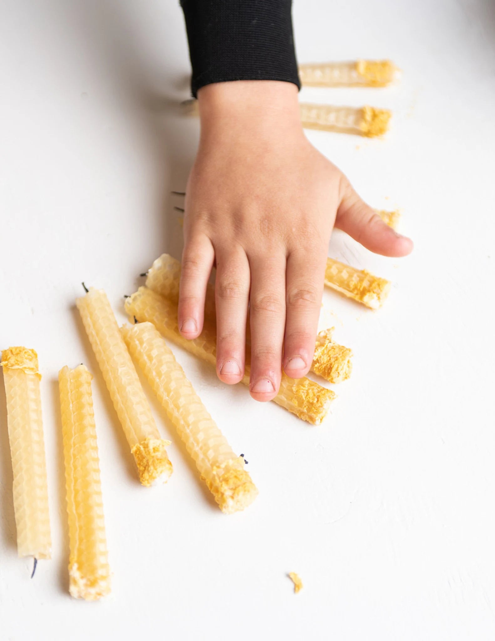 Hand reaching towards yellow beeswax candles on a white surface