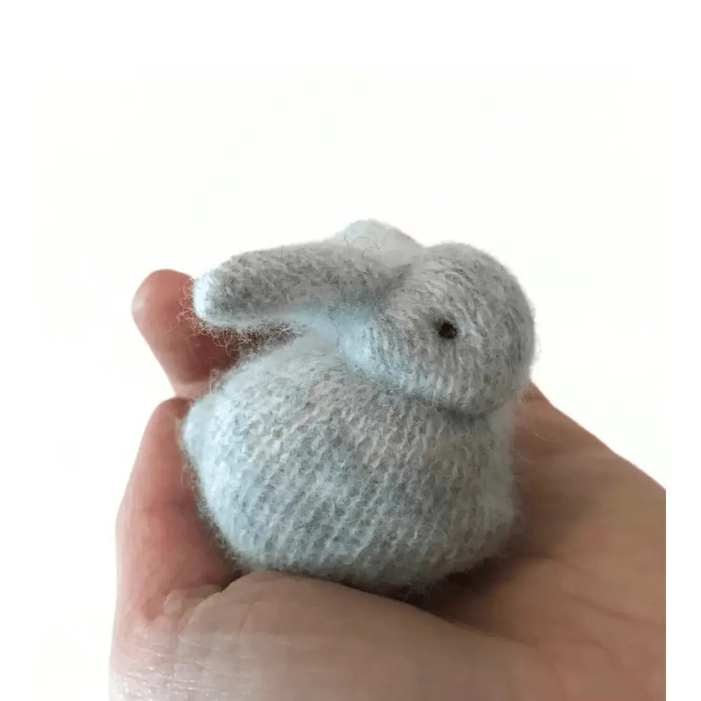 Small knitted bunny held in a hand against a white background