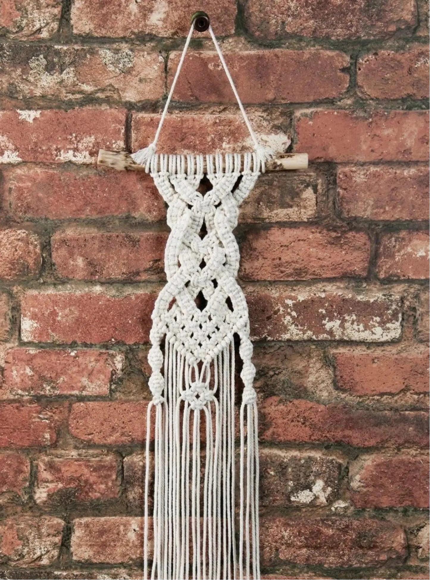 Macrame wall hanging with fringes against a brick wall